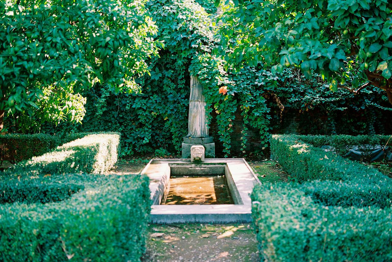 Peaceful garden scene with a stone fountain and lush greenery in Italy.