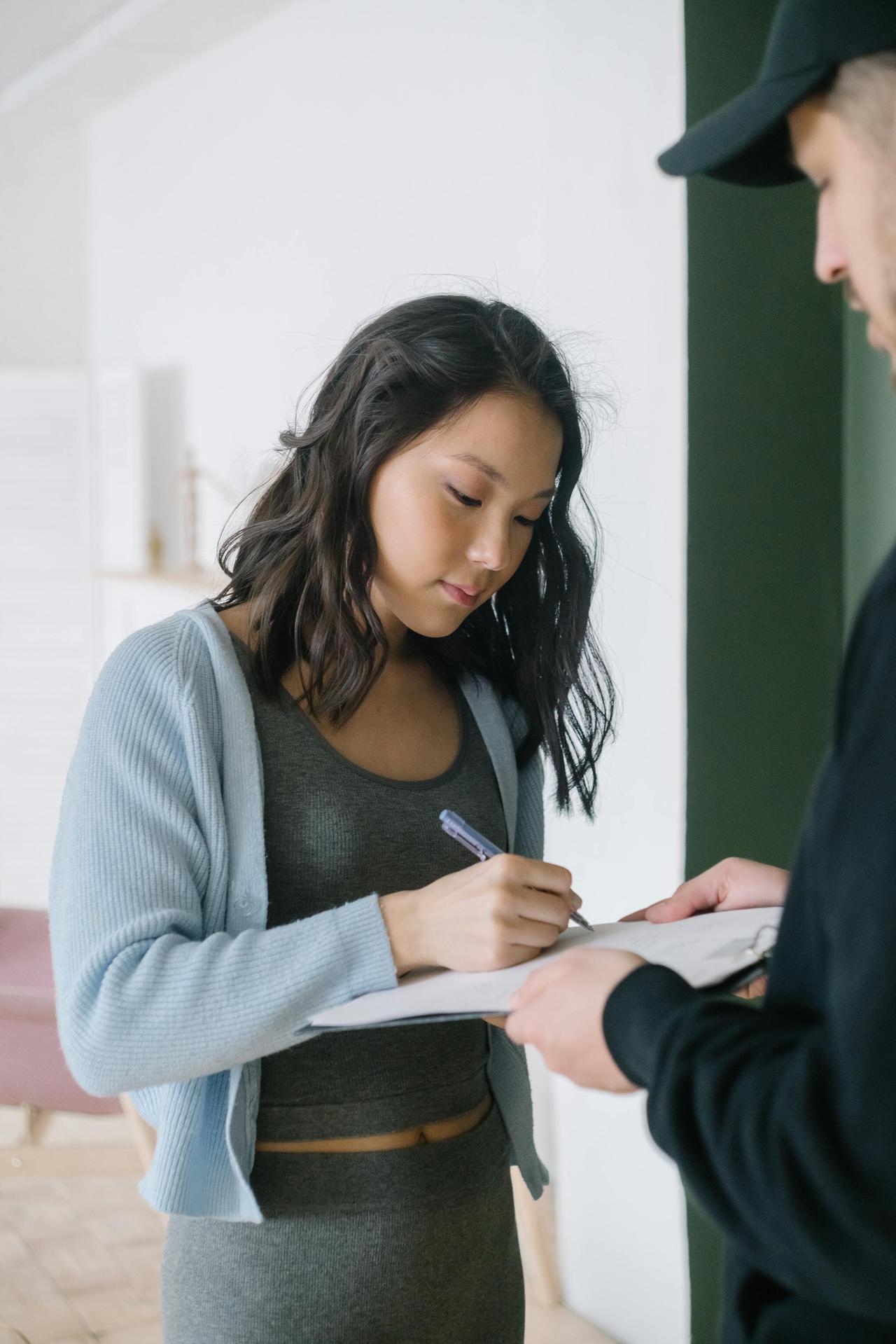 Young woman signing a document indoors, assisted by a man, highlighting a business transaction.