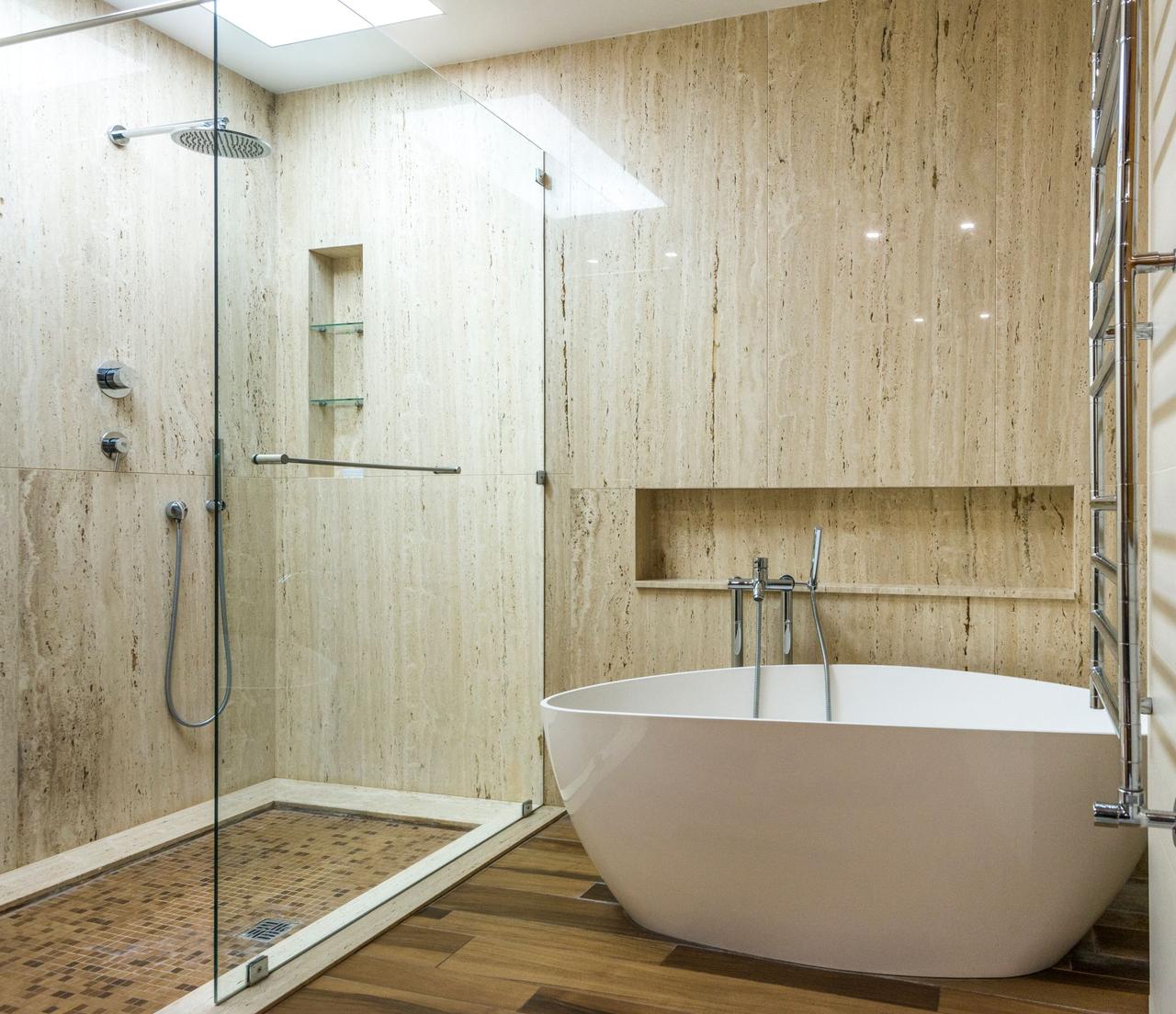 Contemporary bathroom featuring a marble wall, glass shower, and stylish bathtub.