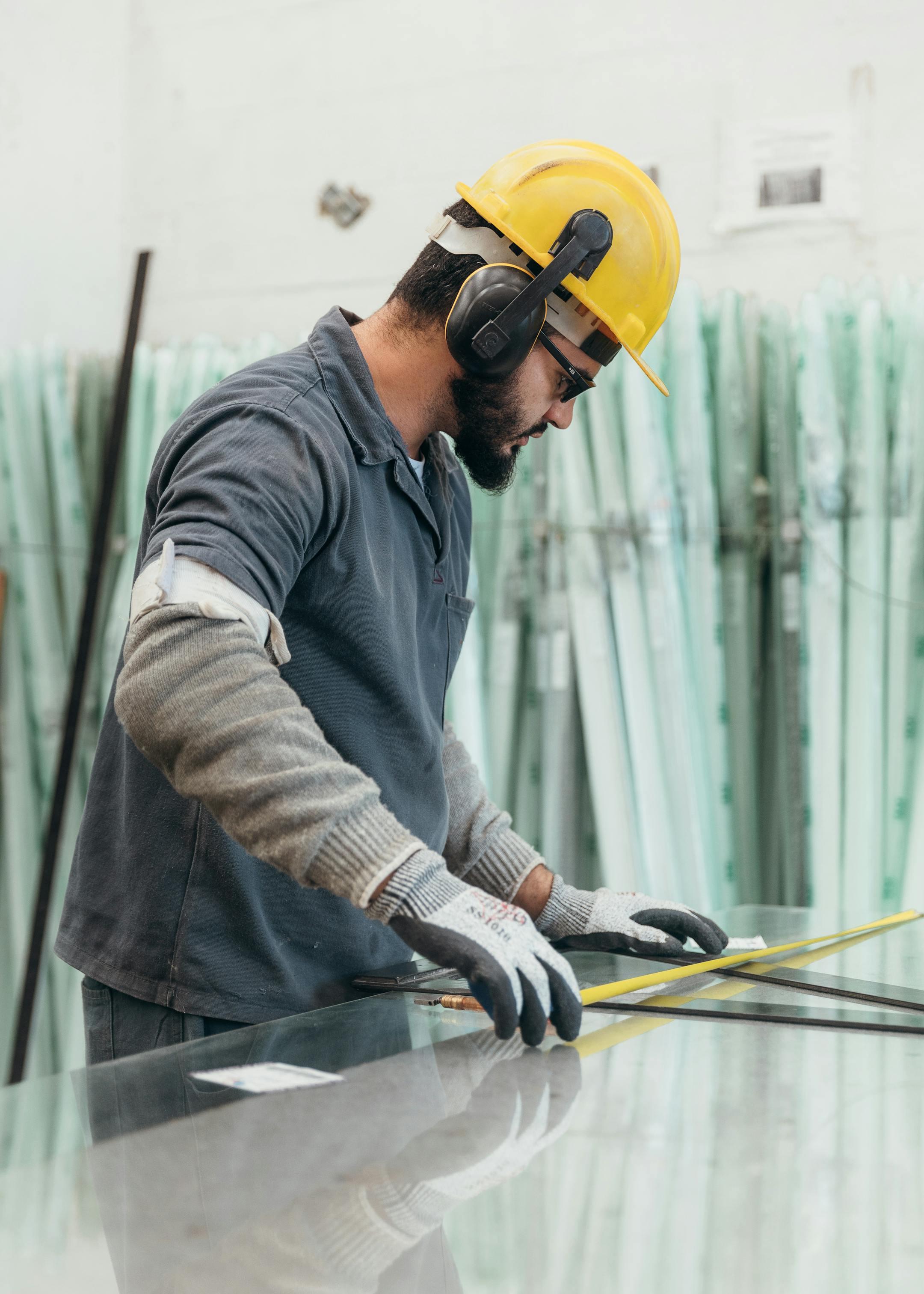 Worker in protective gear measuring glass using a measuring tape indoors.