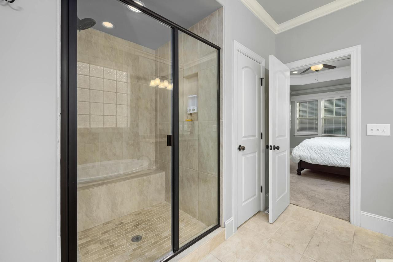 An upscale bathroom featuring a sleek glass shower door, leading to a cozy bedroom with natural lighting.