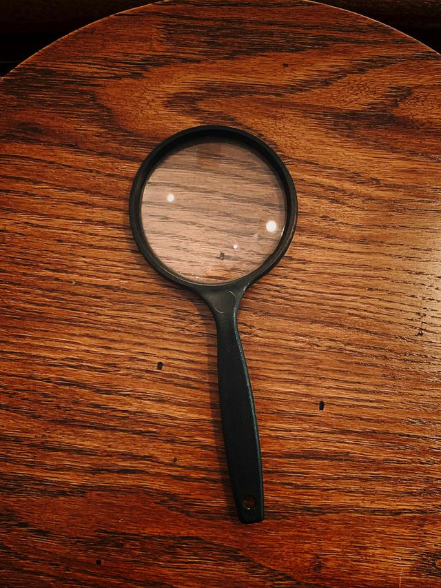 A magnifying glass on a wood table. Our private investigator training courses will teach you how to look at every single detail to succeed as a PI!