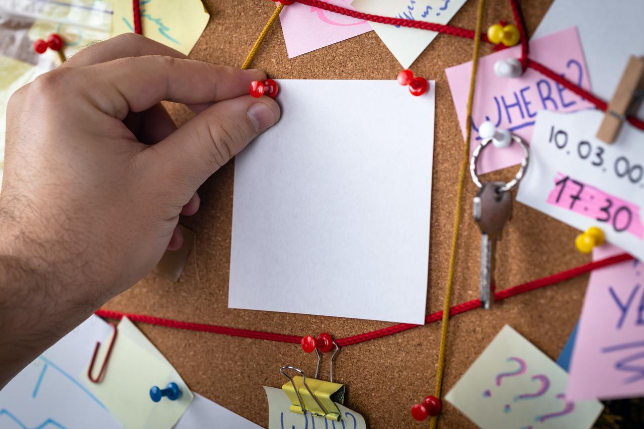 close-up view of a private investigator's board with evidence. In the center is a empty mock up white sheet attached with a red pin