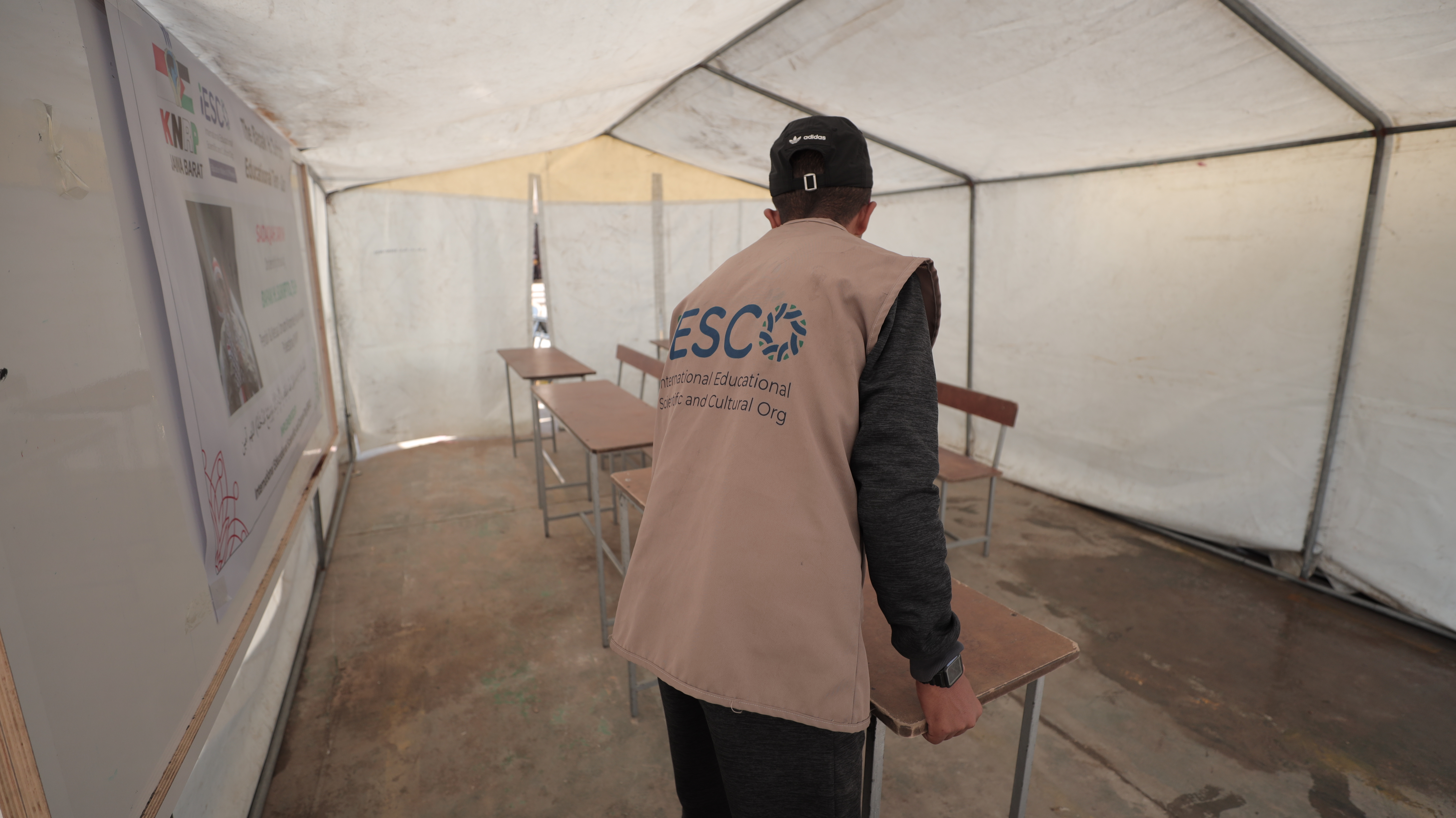 Man placing desks and chairs for students in a tent