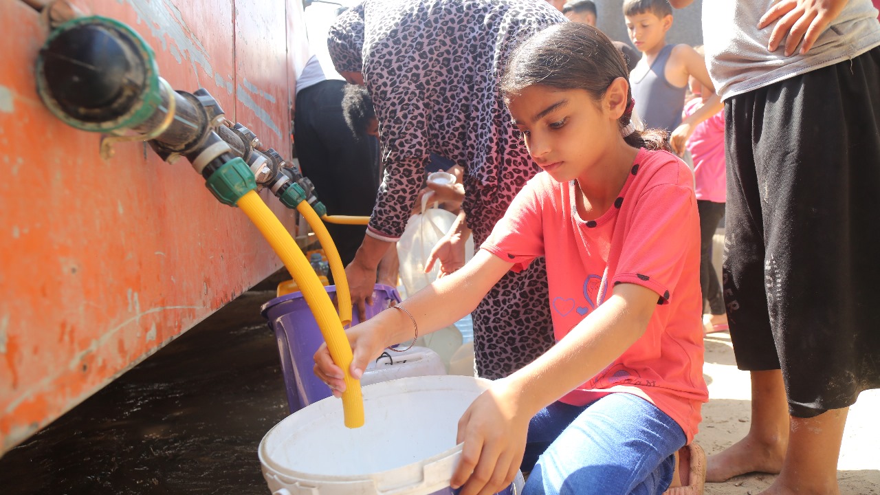 Girl filling bucket with drinking water from truck