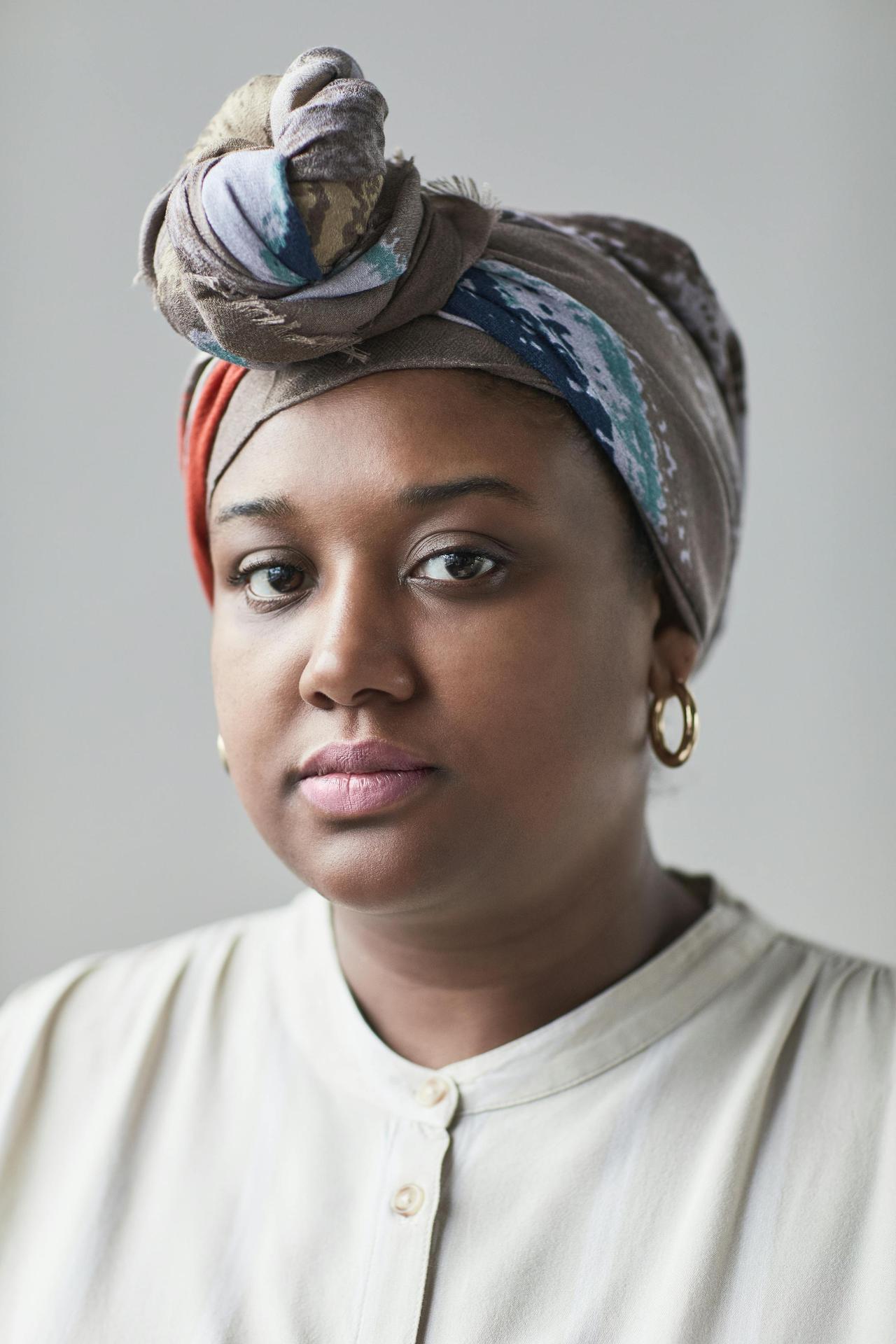 Close-up portrait of an adult woman wearing a multicolored turban with hoop earrings, looking confidently at the camera.