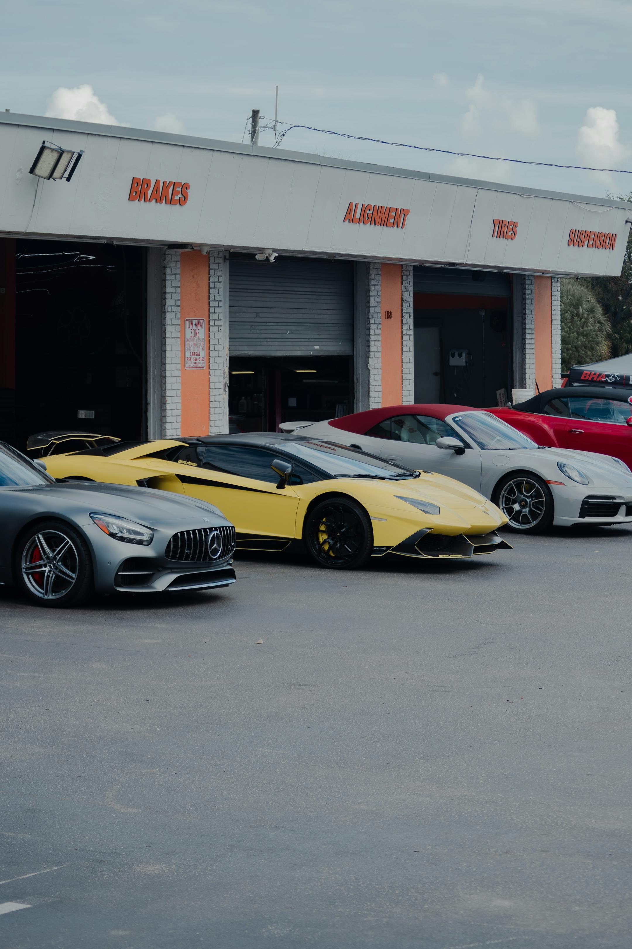 Exotic luxury sports cars parked outside an auto repair shop under a cloudy sky.