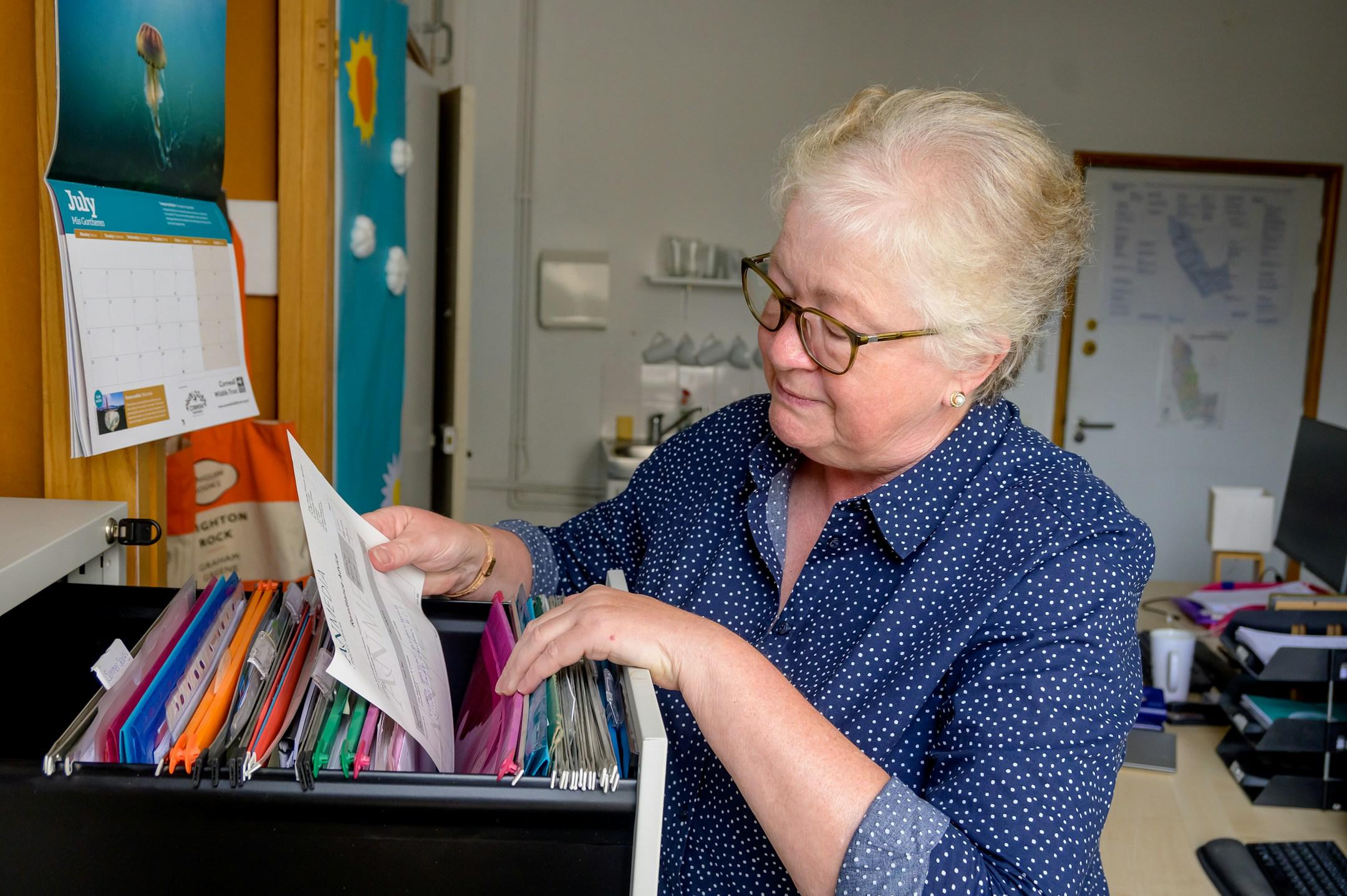 An older woman working, pulling out some files from a drawer.