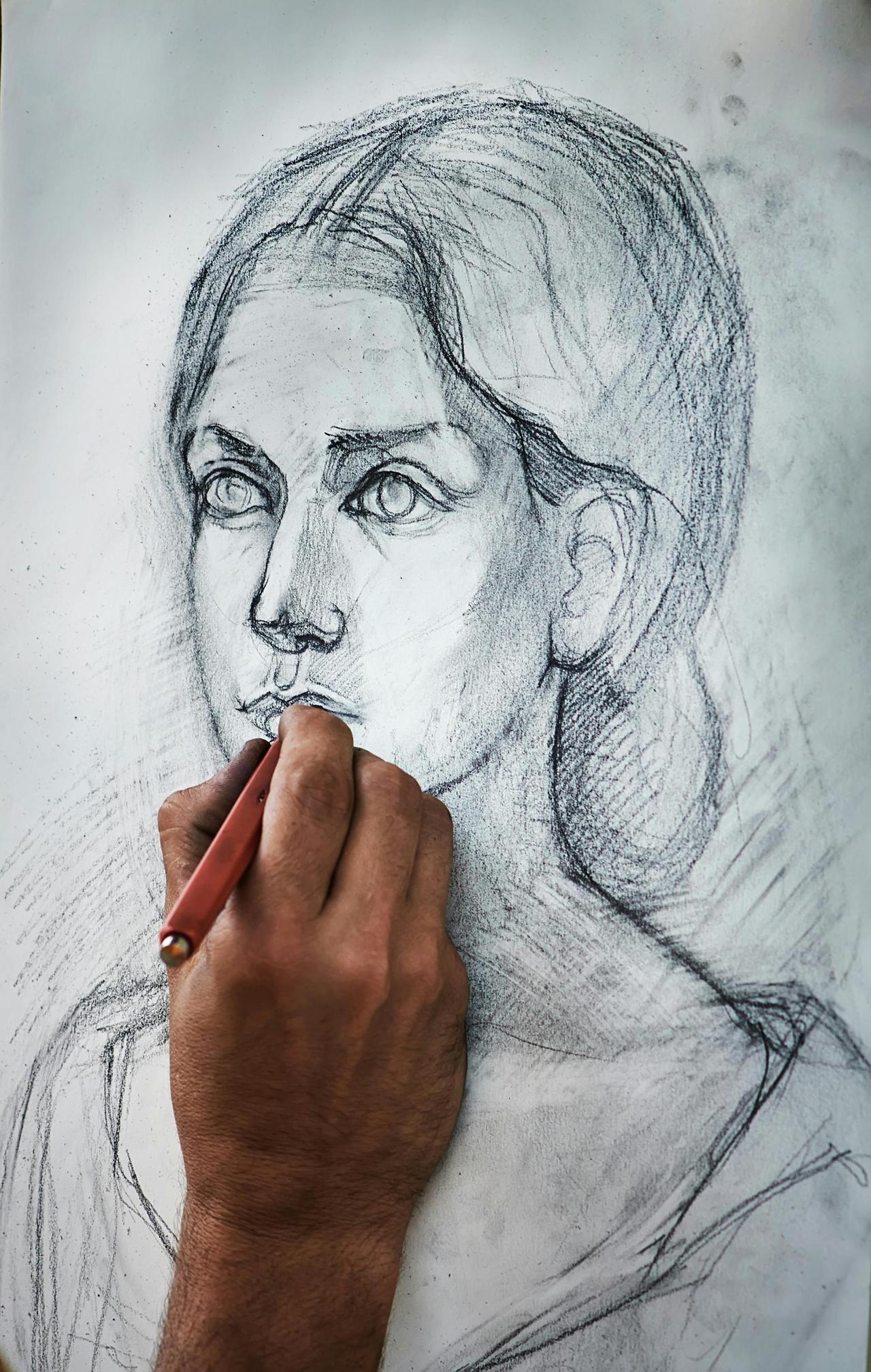 Crop unrecognizable person drawing portrait of charming woman with pencil on canvas in art studio