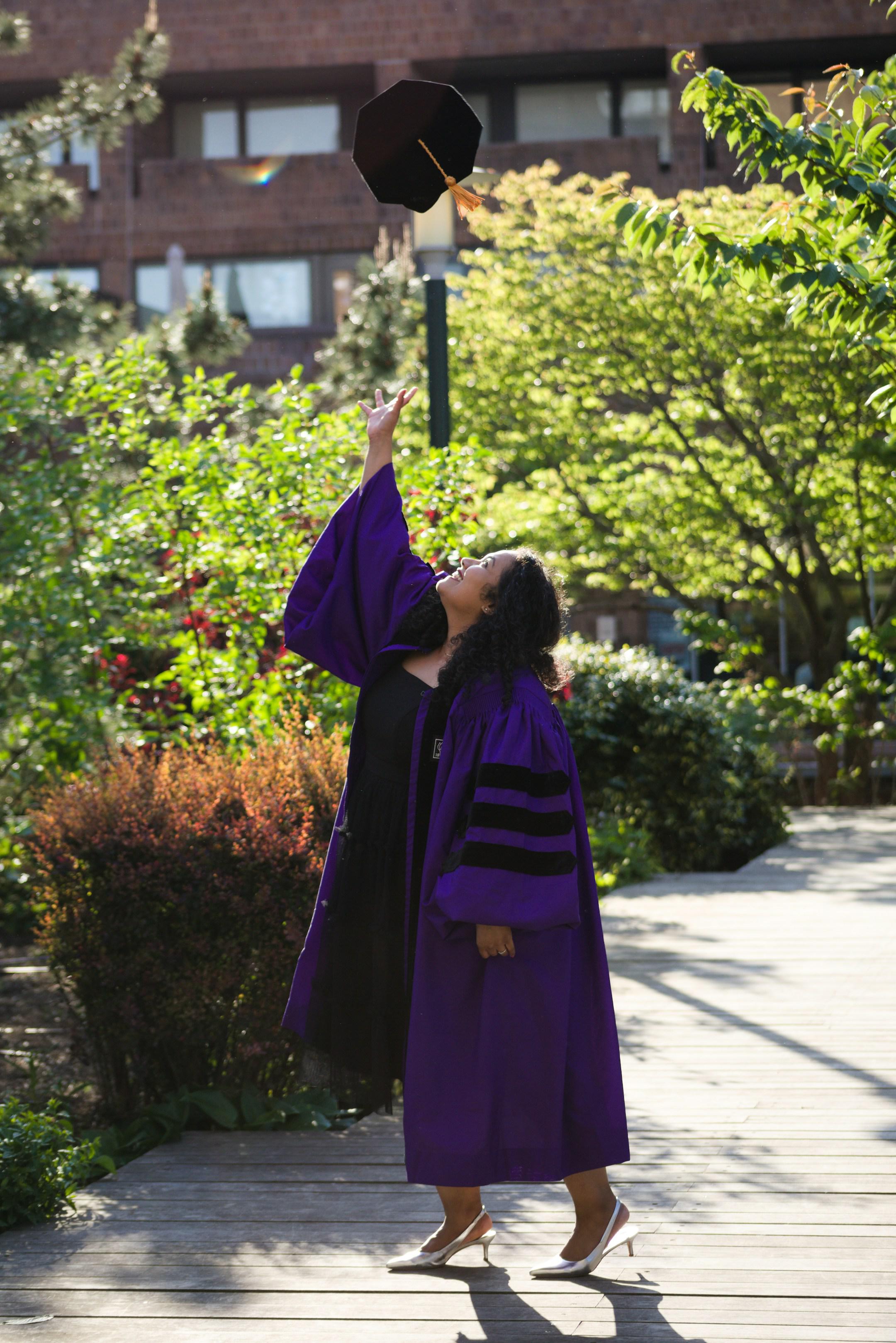 A graduate joyfully tosses her cap in the air, celebrating her academic achievement in her purple graduation gown.