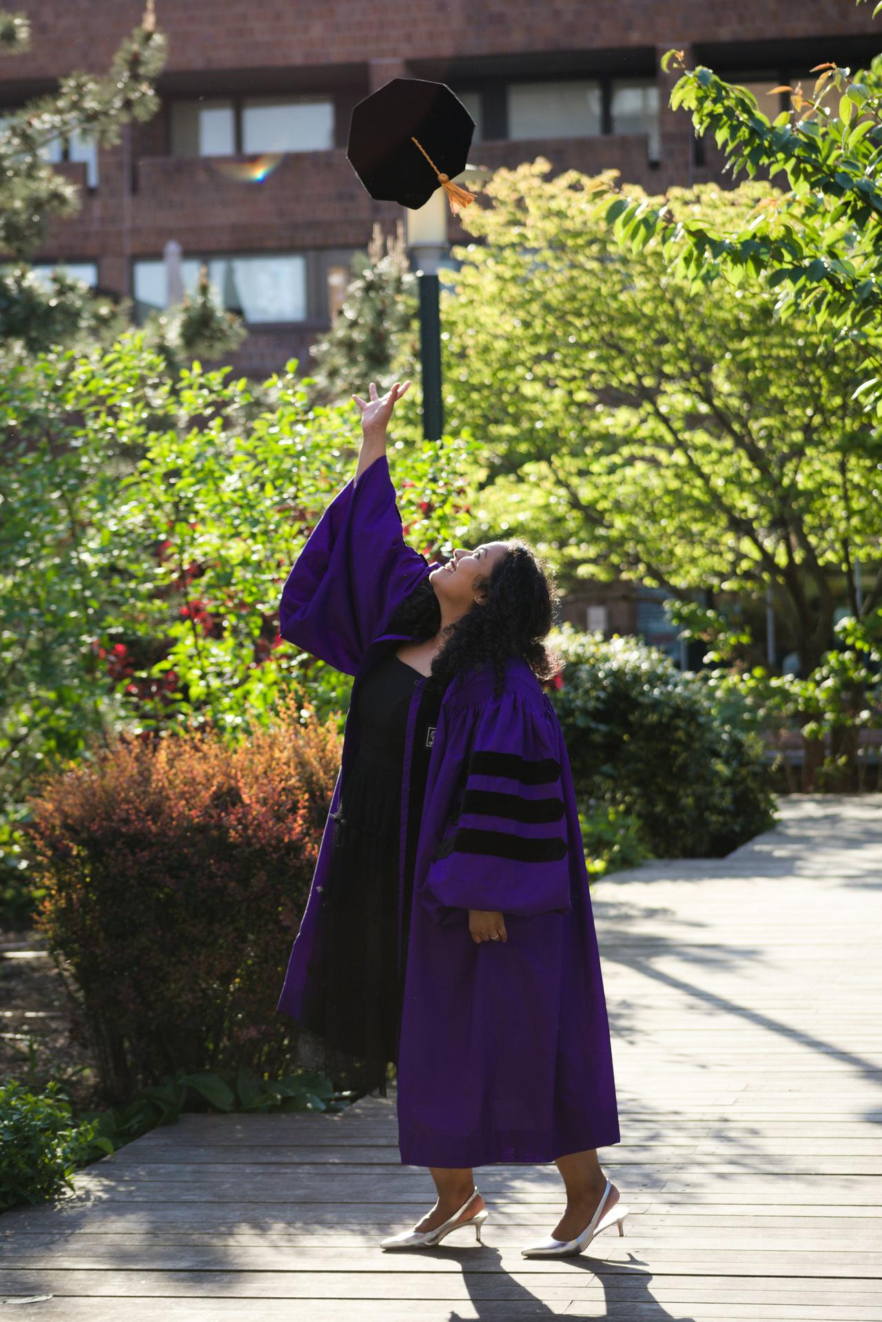 A graduate joyfully tosses her cap in the air, celebrating her academic achievement in her purple graduation gown.