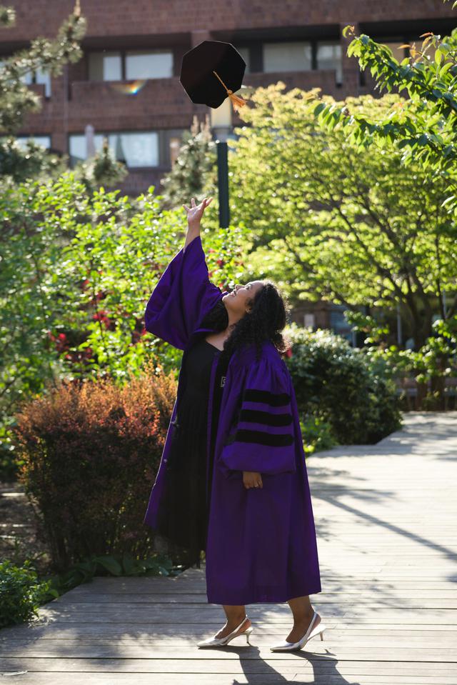 A graduate joyfully tosses her cap in the air, celebrating her academic achievement in her purple graduation gown.