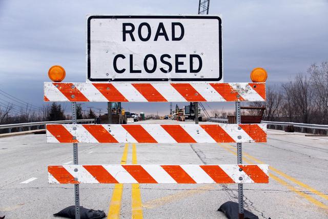 A road closed sign with barricade highlights caution on a suburban highway.