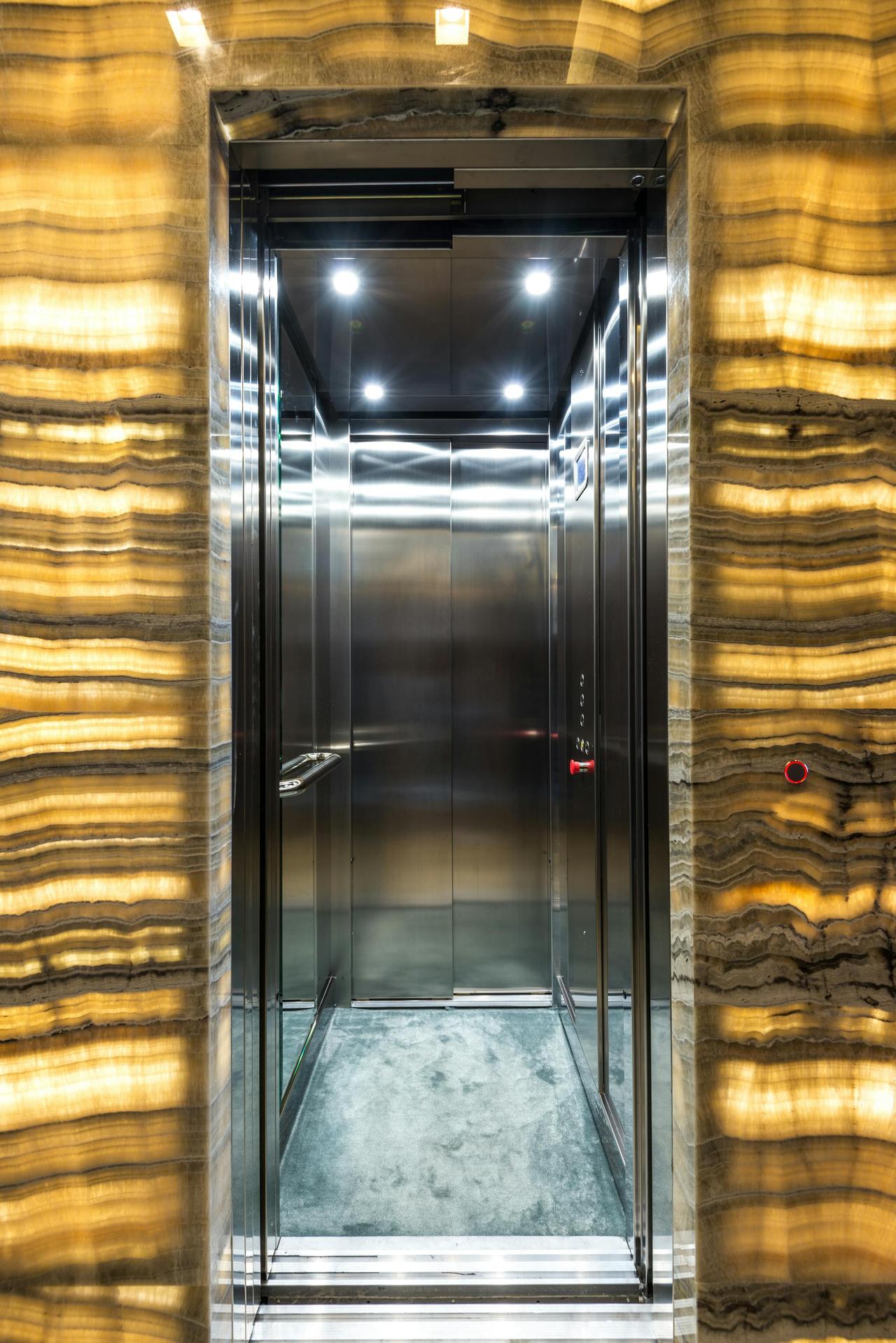 Brightly lit stainless steel elevator with marble walls and modern lighting design.