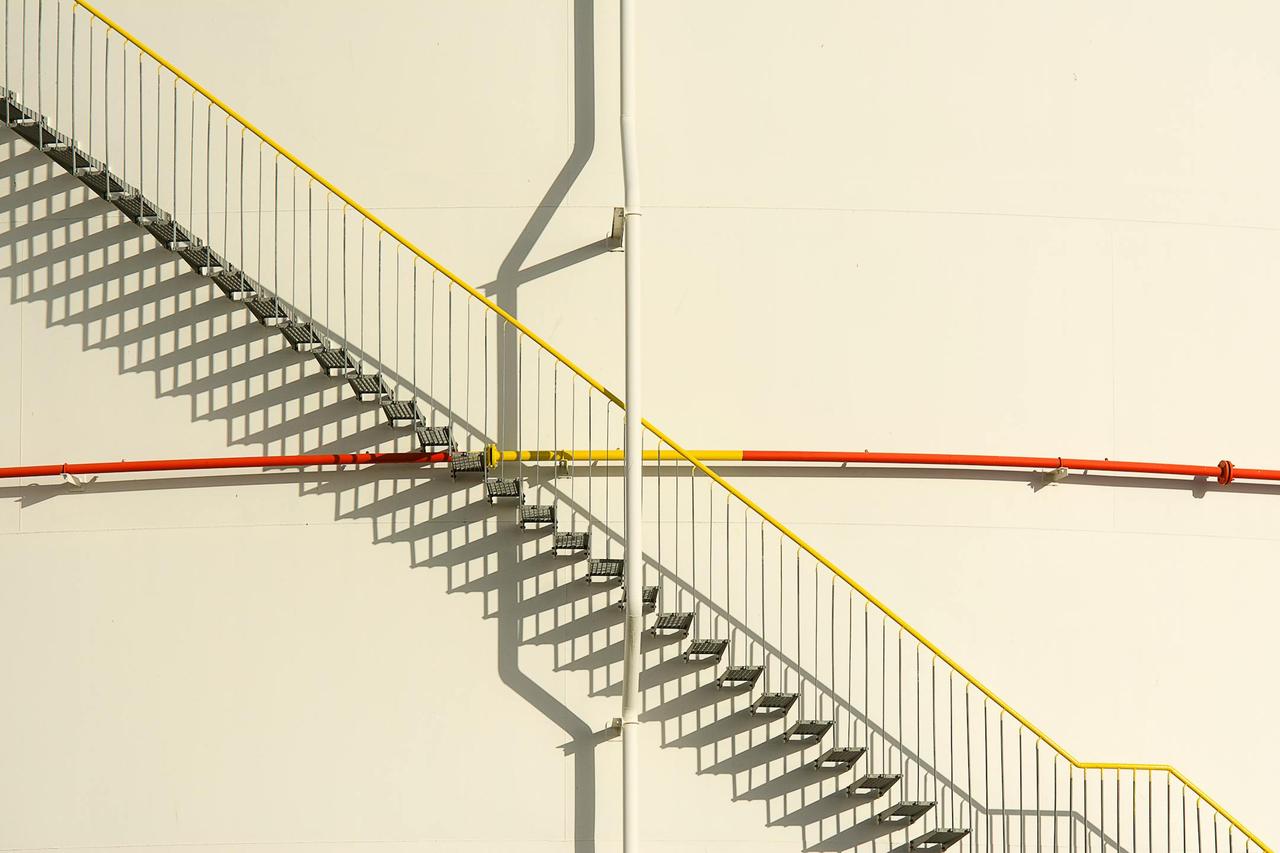 Metal staircase on a concrete wall with dramatic shadows and piping.