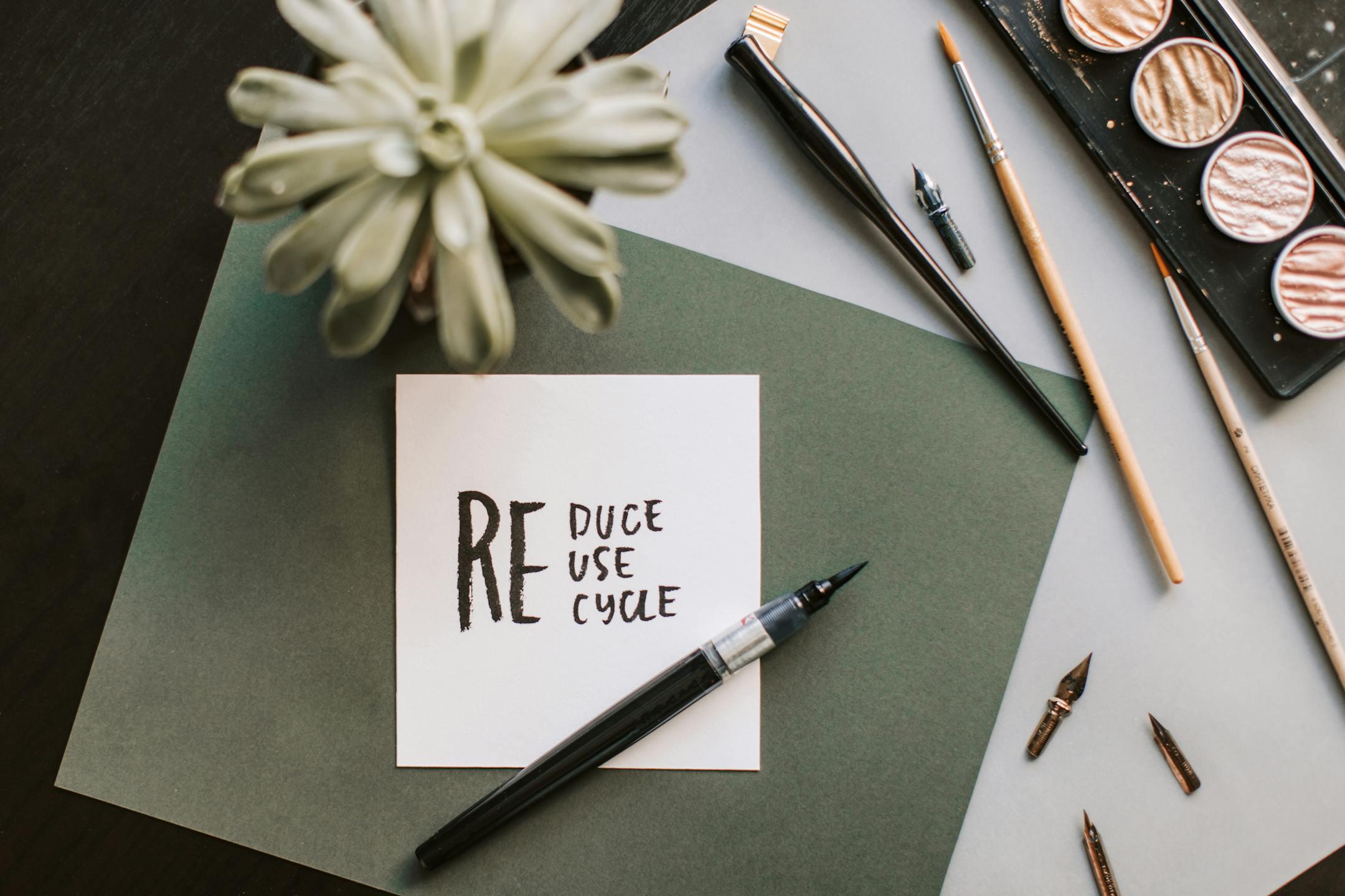 Flat lay of art materials featuring a recycle-themed note and calligraphy tools. <br>Discover recycling and waste management options in Conroe, TX. Learn how green cleaning and eco-friendly habits create a cleaner, healthier, sustainable future