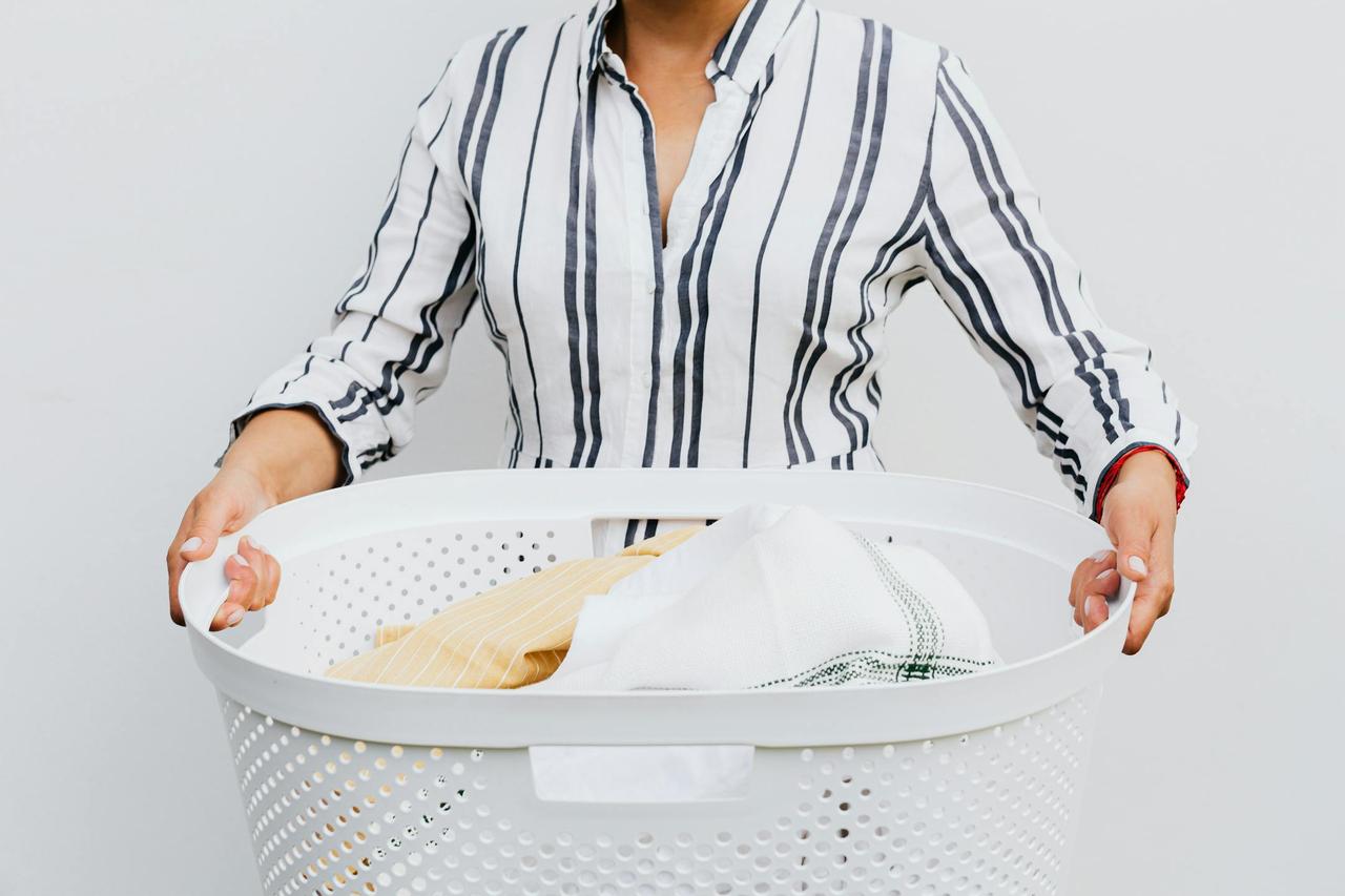 A woman holding a laundry basket filled with clothes against a plain white background.