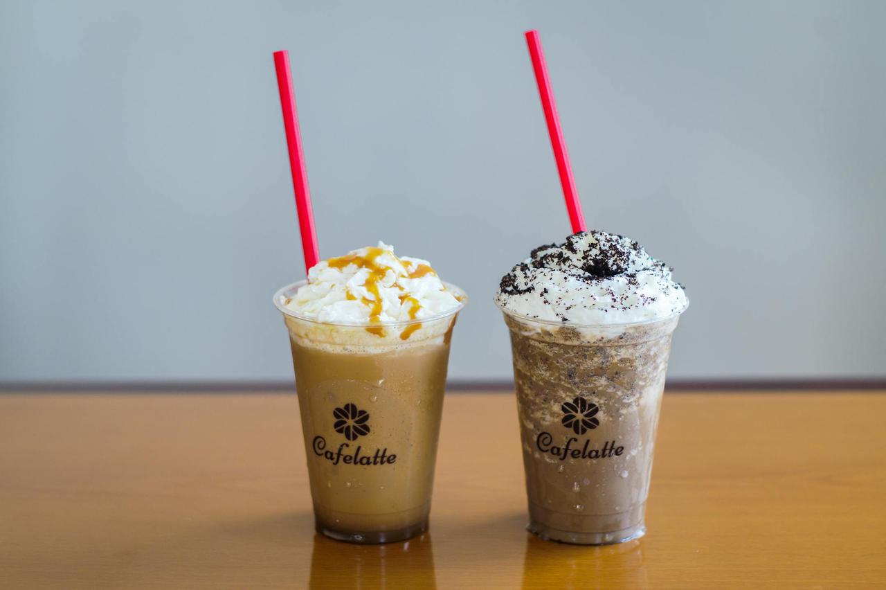 Two cold coffee drinks with whipped cream and toppings, featuring red straws and branded cups on a wooden table.
