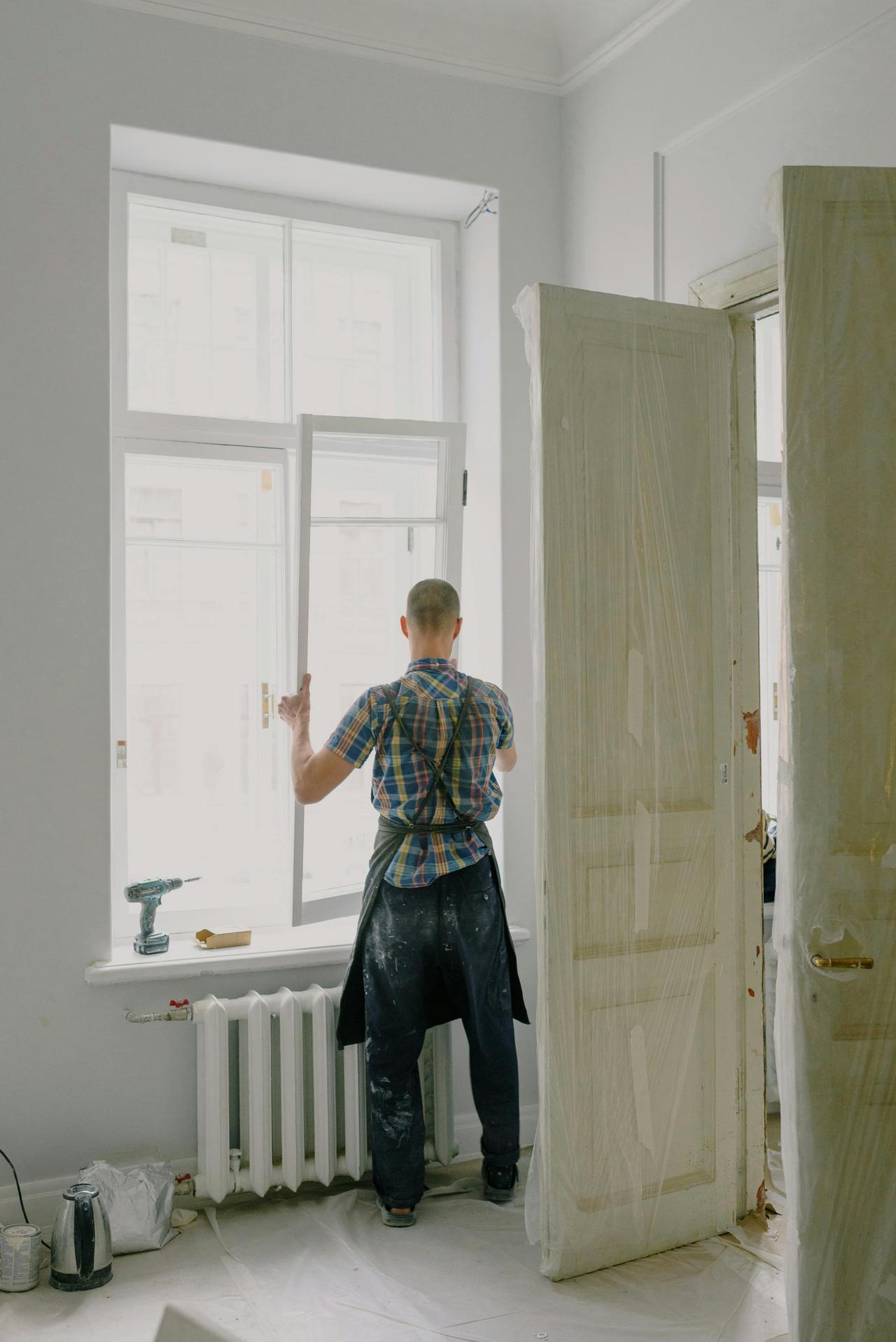 Full-length view of a handyman fixing a modern window in a bright room.