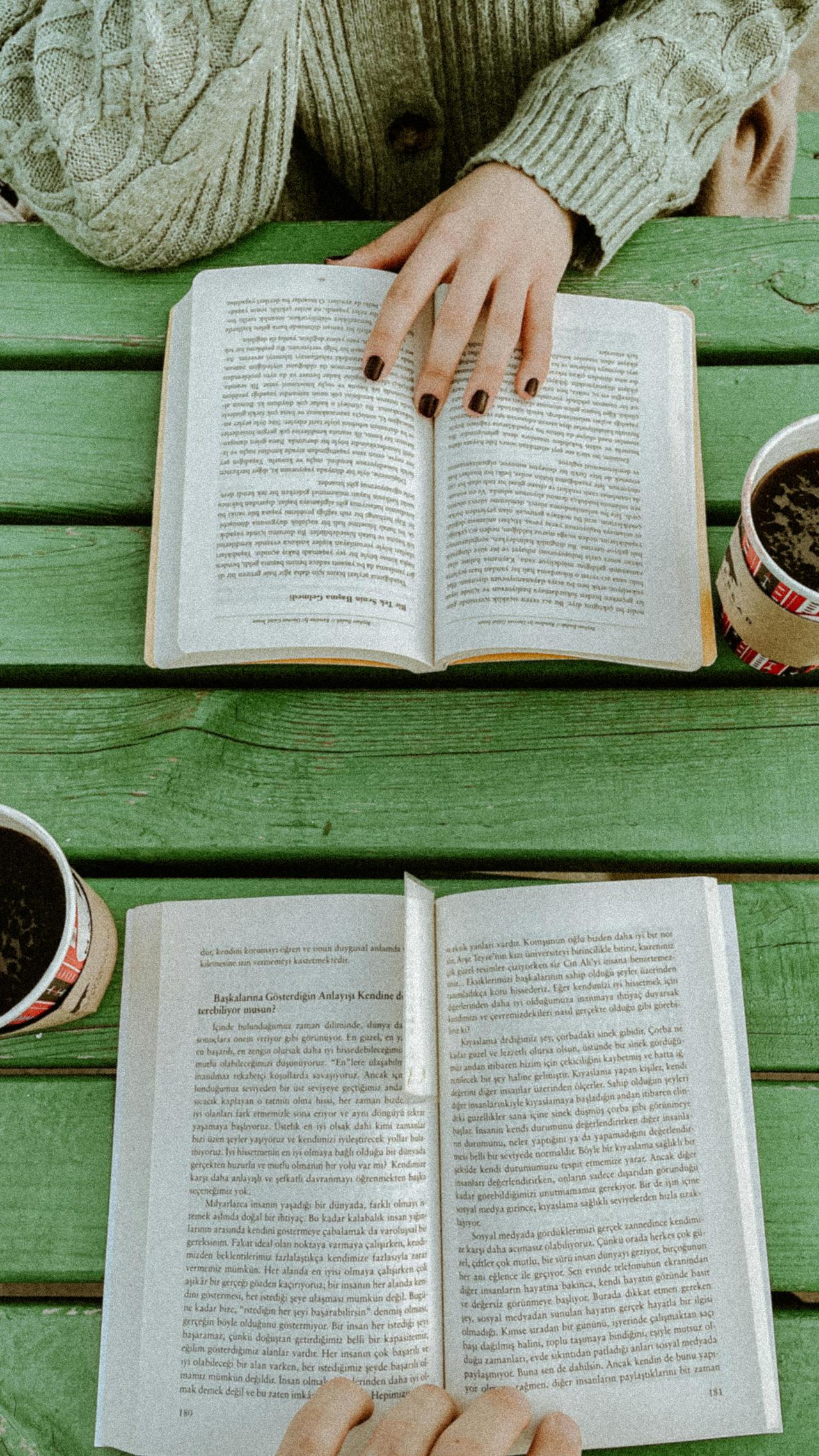 Cozy outdoor reading session with books and coffee on a green table in Antalya.