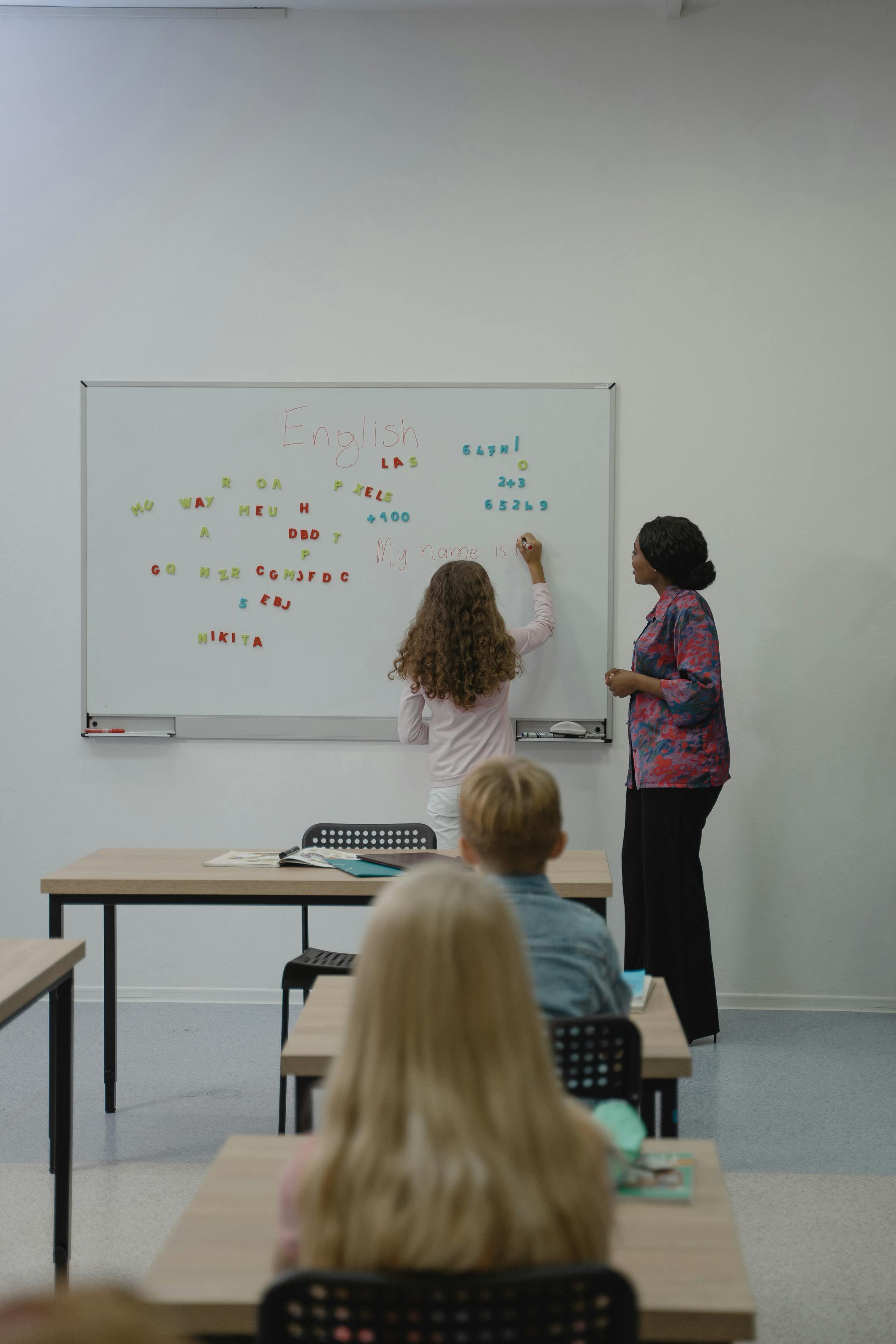 Teacher instructing diverse students with magnetic letters on a classroom whiteboard.