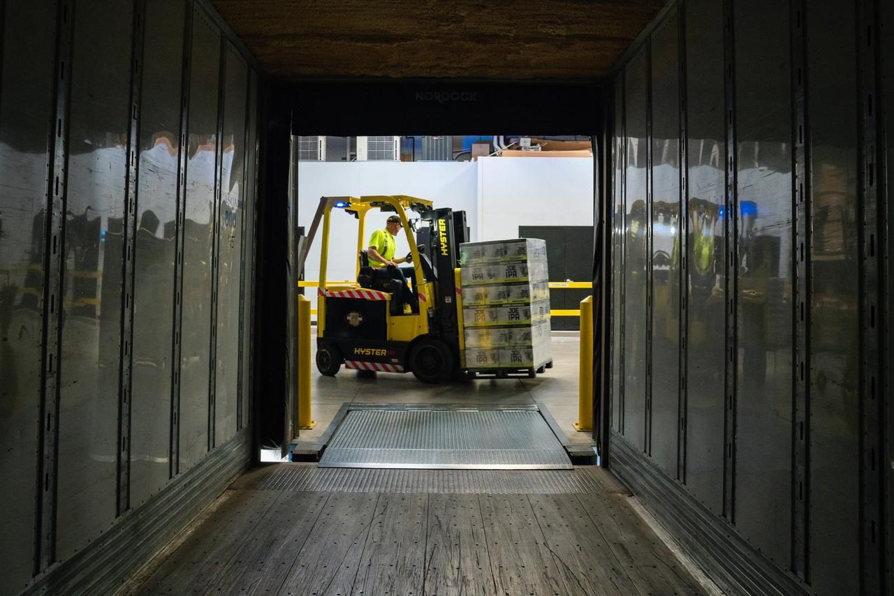 A view down a tunnel of a man in a neon shirt operatin a forklift carrying boxes stacked on a pallet. An OSHA inspection checklist will ensure each aspect of this process is up to code.