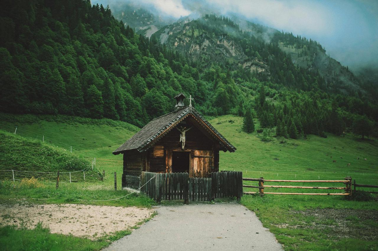 A charming wooden cabin set in a lush green valley beneath misty mountains, showcasing rural serenity.