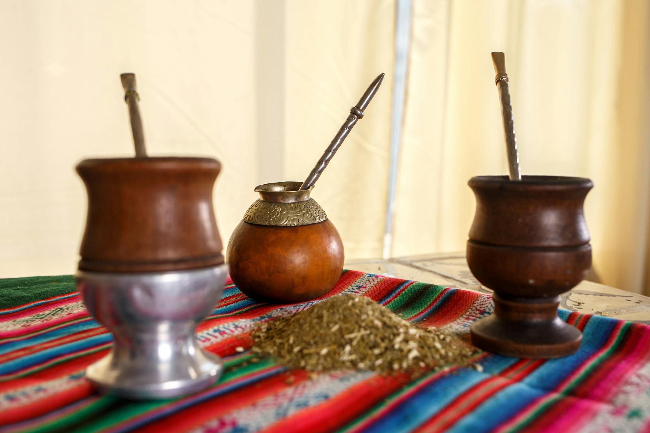 Three traditional yerba mate cups with bombillas on a vibrant cloth indoors.