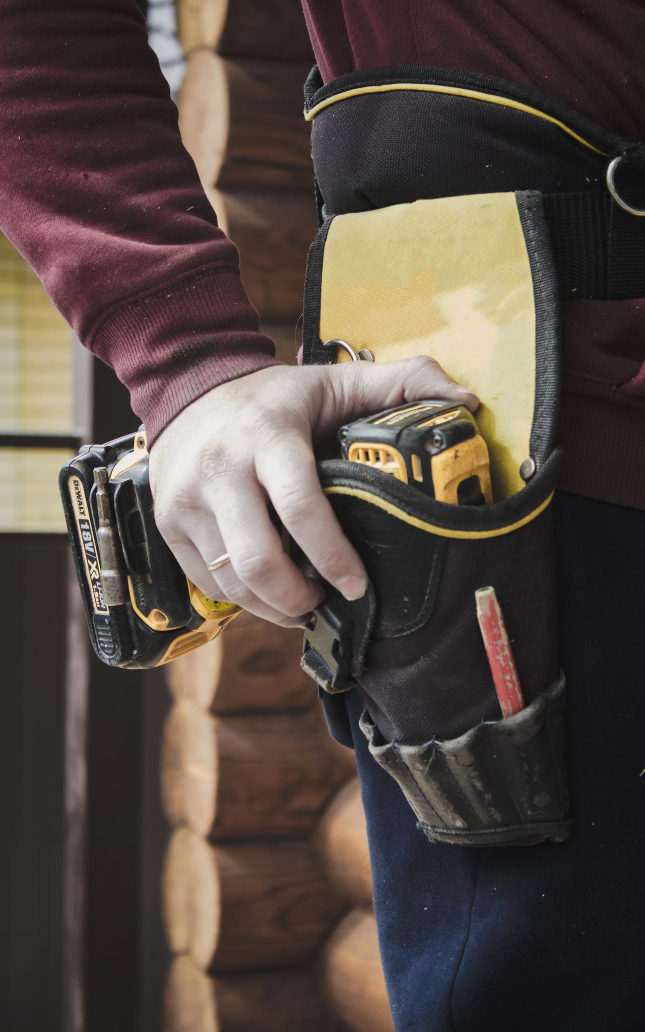 Satisfied worker is drilling wall. Builder is working construction site. Wooden house