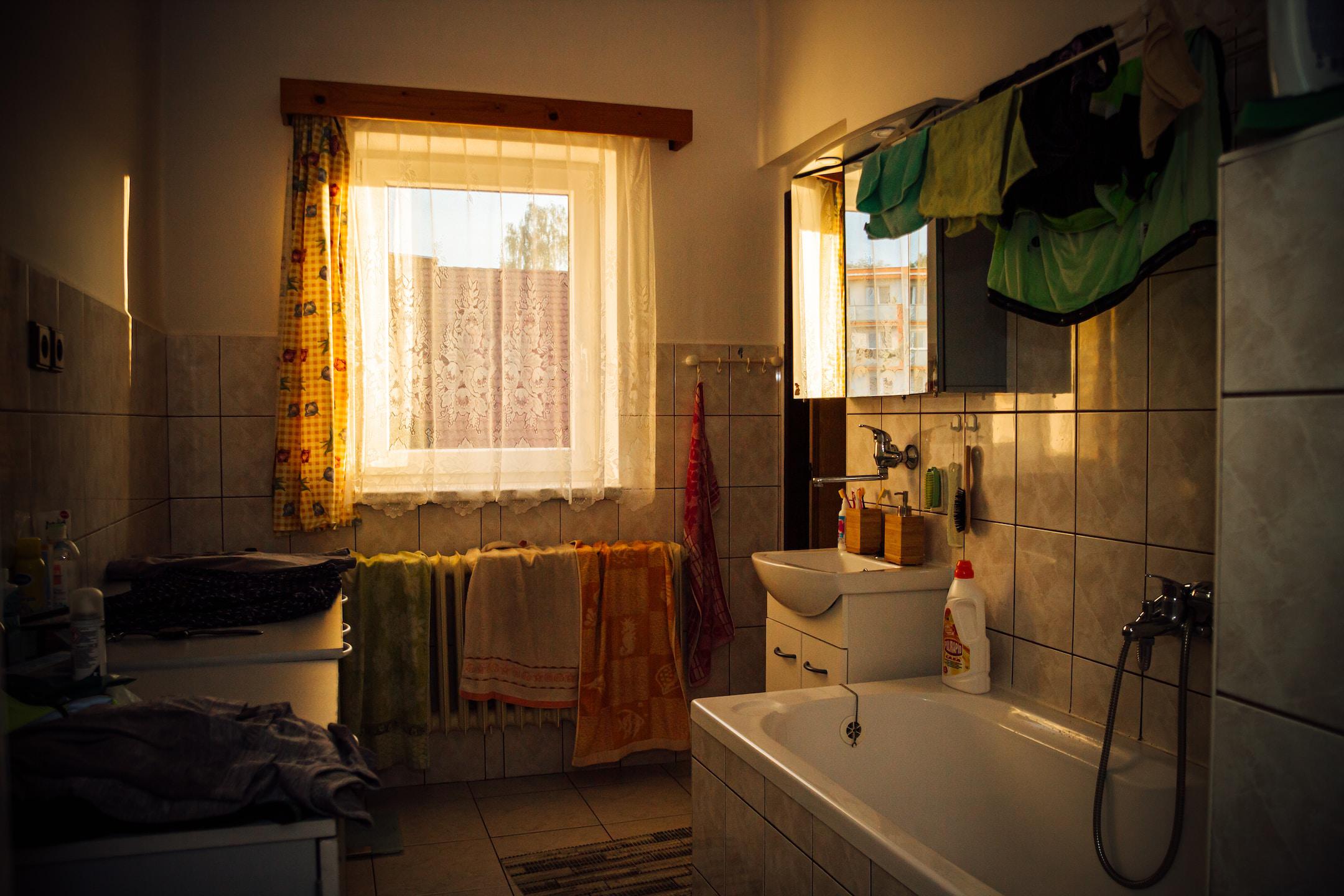 Messy bathroom during sunset. Clothes and towels are drying.