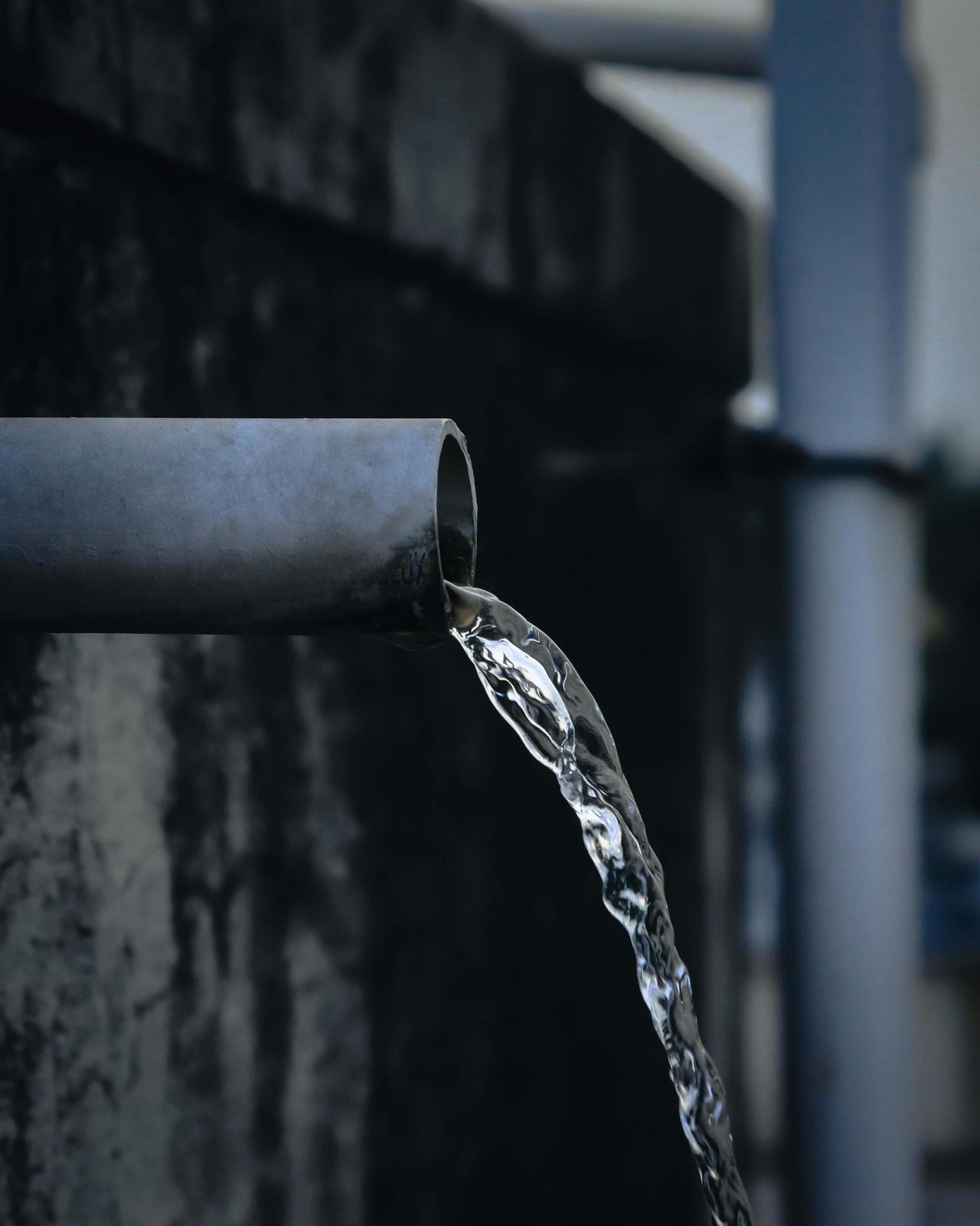 Close-up view of water pouring from an industrial metal pipe, captured outdoors.