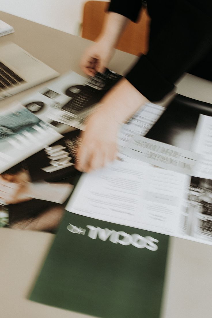 Hands arranging editorial and business materials on a worktable.