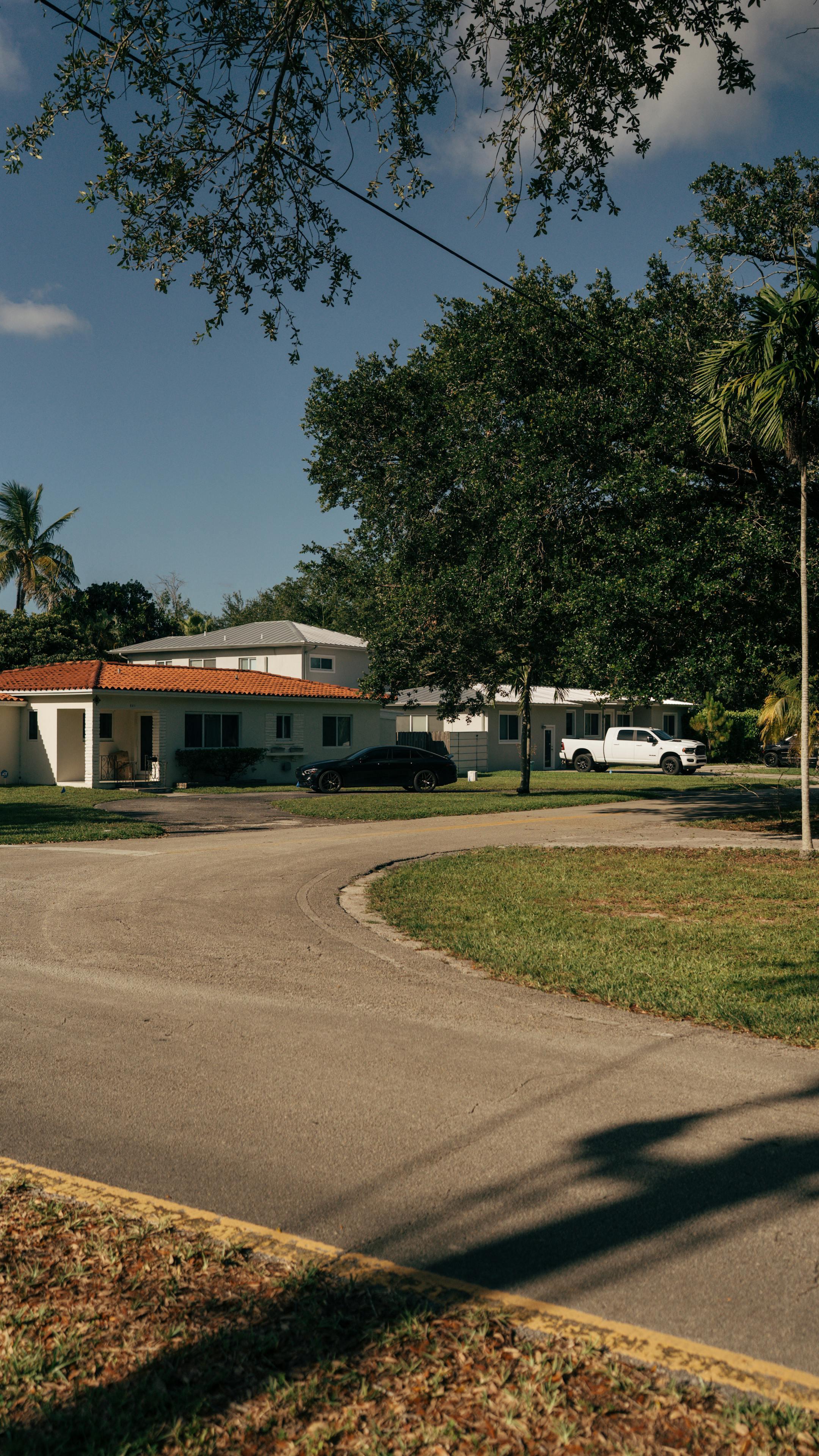 Peaceful suburban street with houses, trees, and cars under a clear sky.