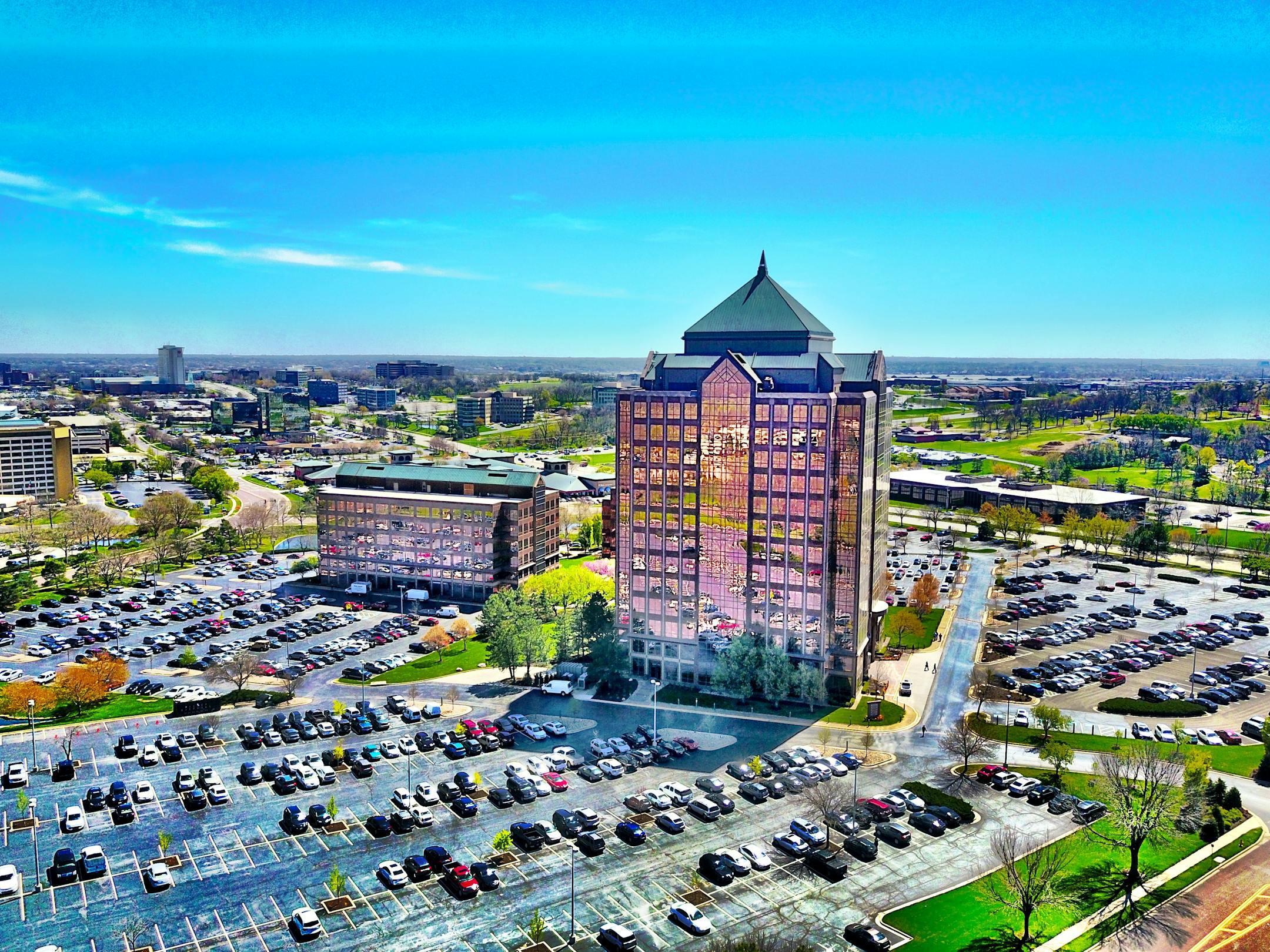 Bird's-eye view of a modern skyscraper and parking lot in Overland Park, KS, under a clear blue sky.