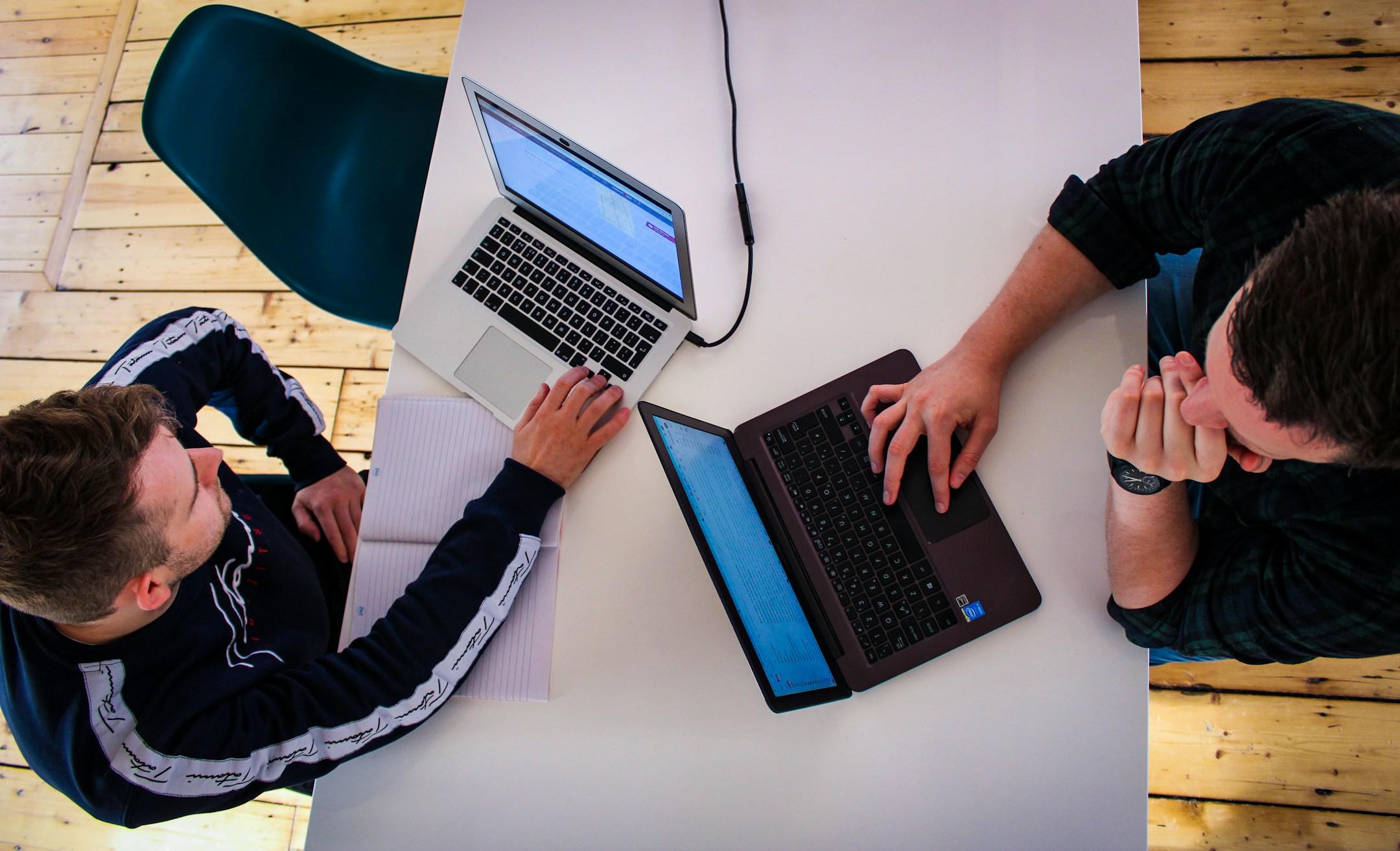 Digital marketing team in office working and reviewing client work on laptops on white board room table and wooden floors