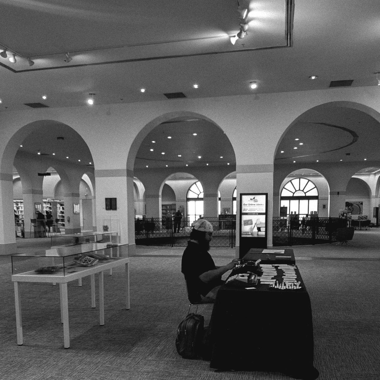 Black-and-white photograph of Chris typing poems at a table inside a library