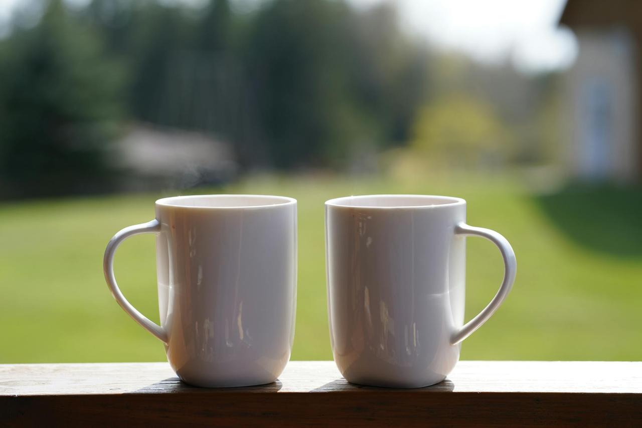 A serene outdoor setting featuring two white mugs on a wooden ledge, perfect for showcasing coffee moments.