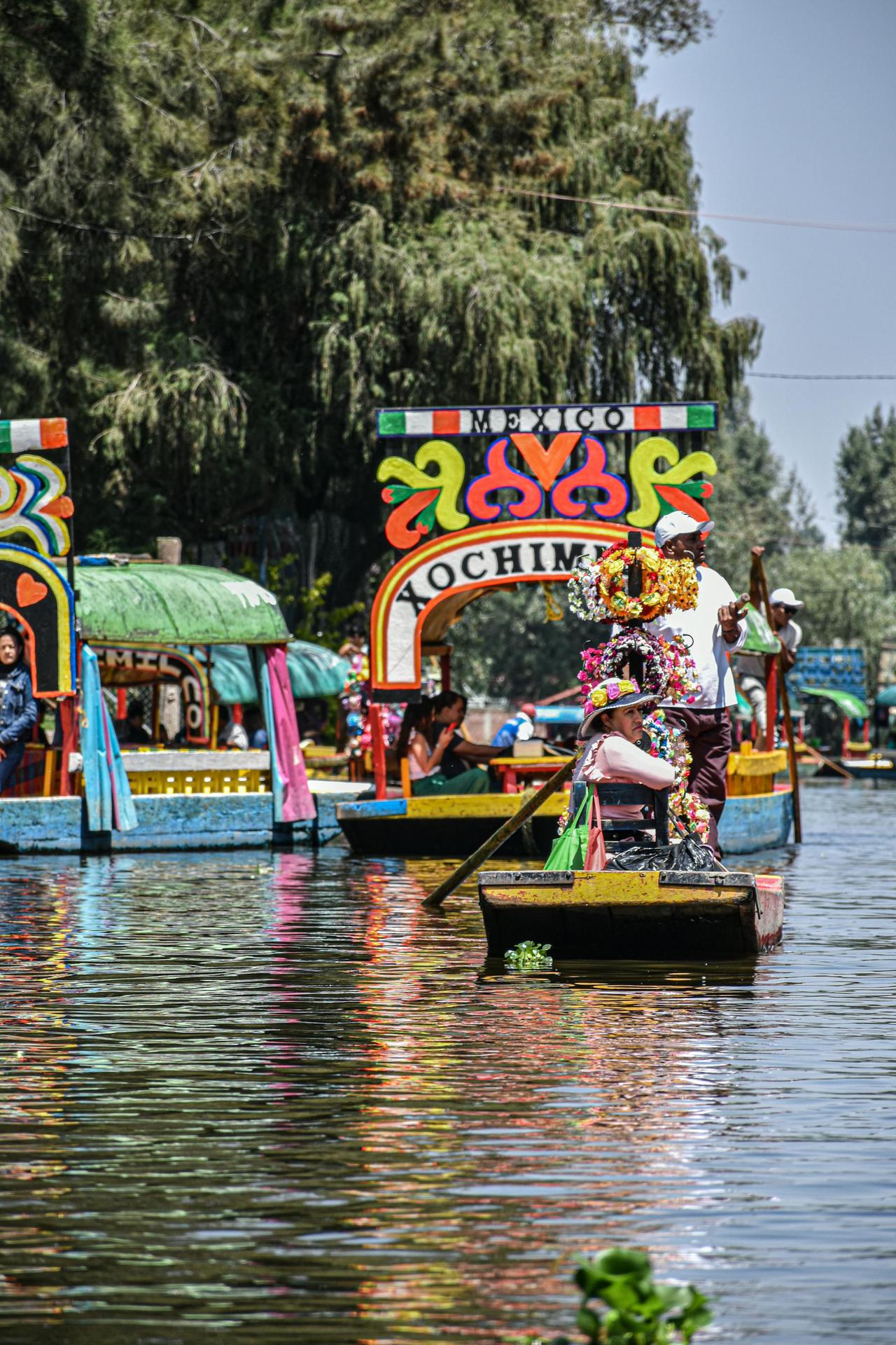 Vibrant trajineras navigating the serene Xochimilco canals in Mexico City on a sunny day.