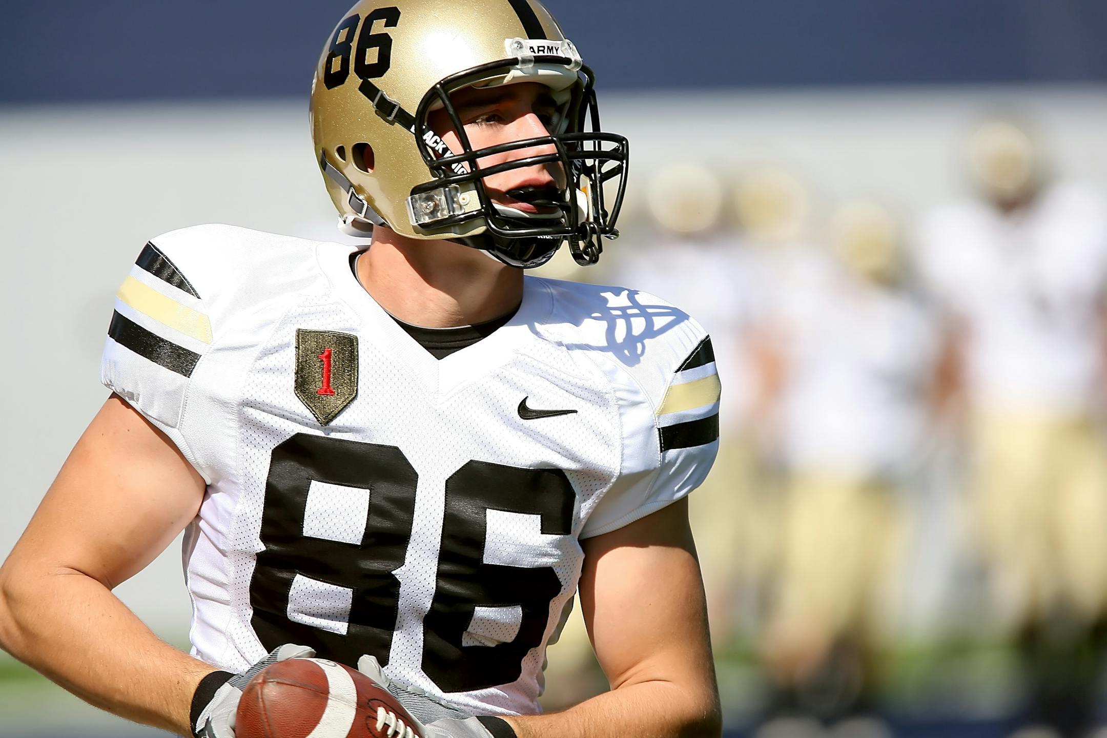 Focused college football player in uniform holding a football during a game.