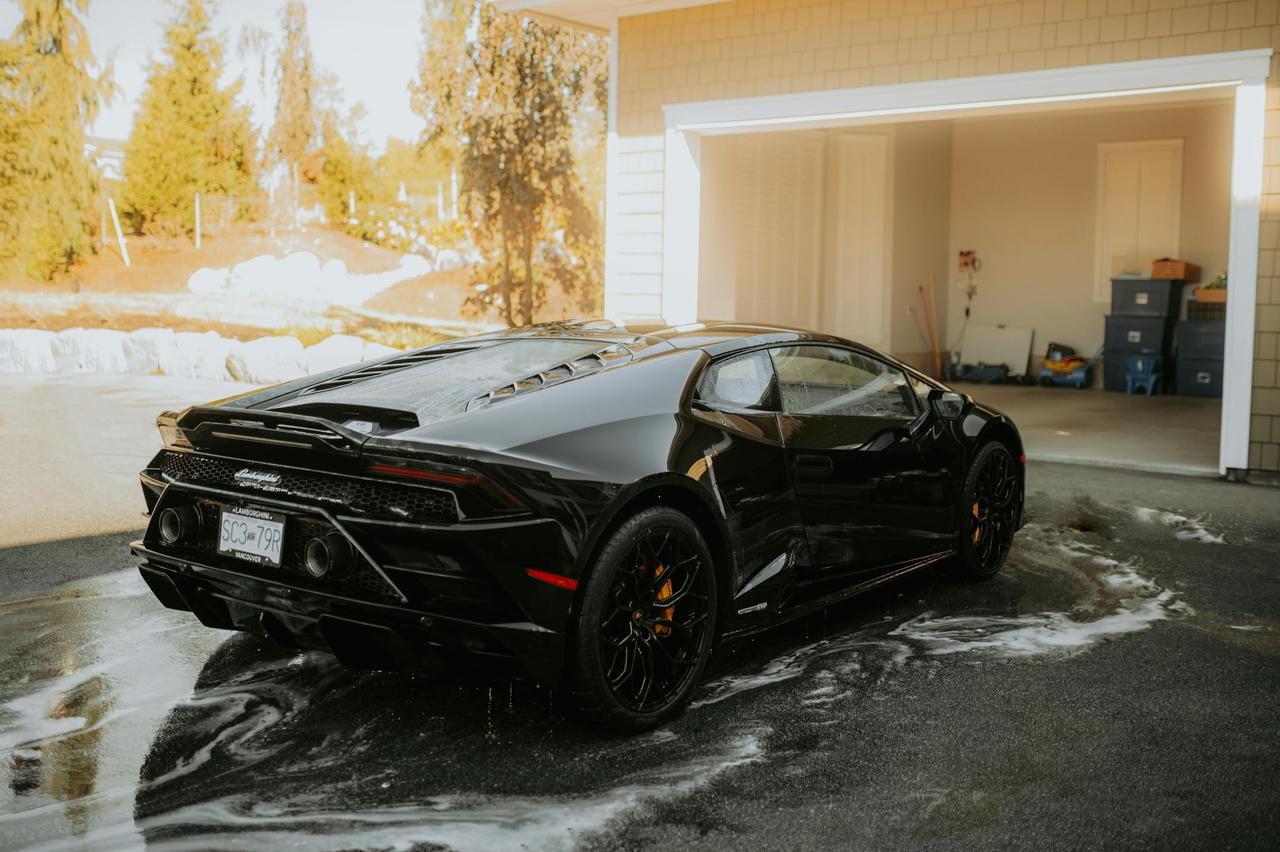 High-end Lamborghini sports car being washed at a sunny outdoor location.