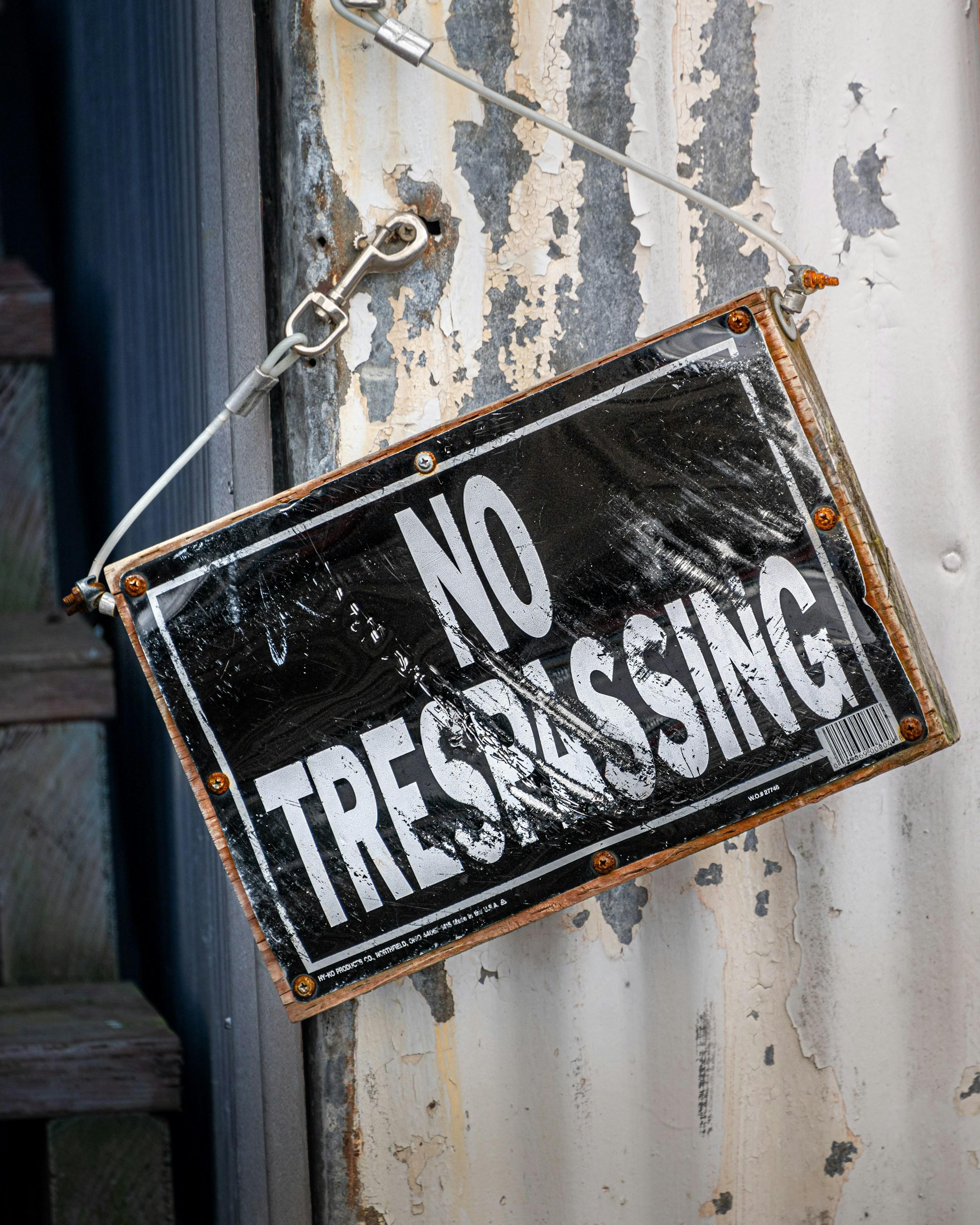 A weathered "No Trespassing" sign hangs on a rusted metal surface, evoking a gritty, industrial feel. Can be used for security, cyber security or any situation where breaking barriers (or not breaking them!) is important.