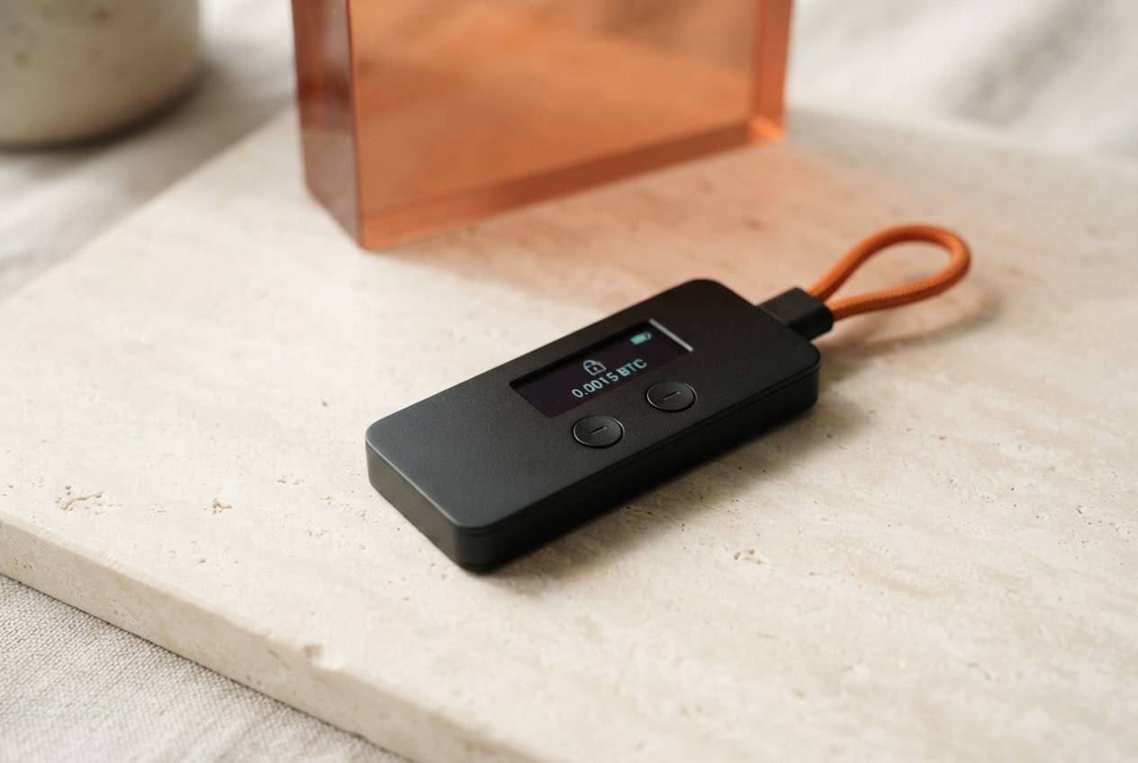 A compact hardware wallet resting on a warm stone surface beside an orange accent cable