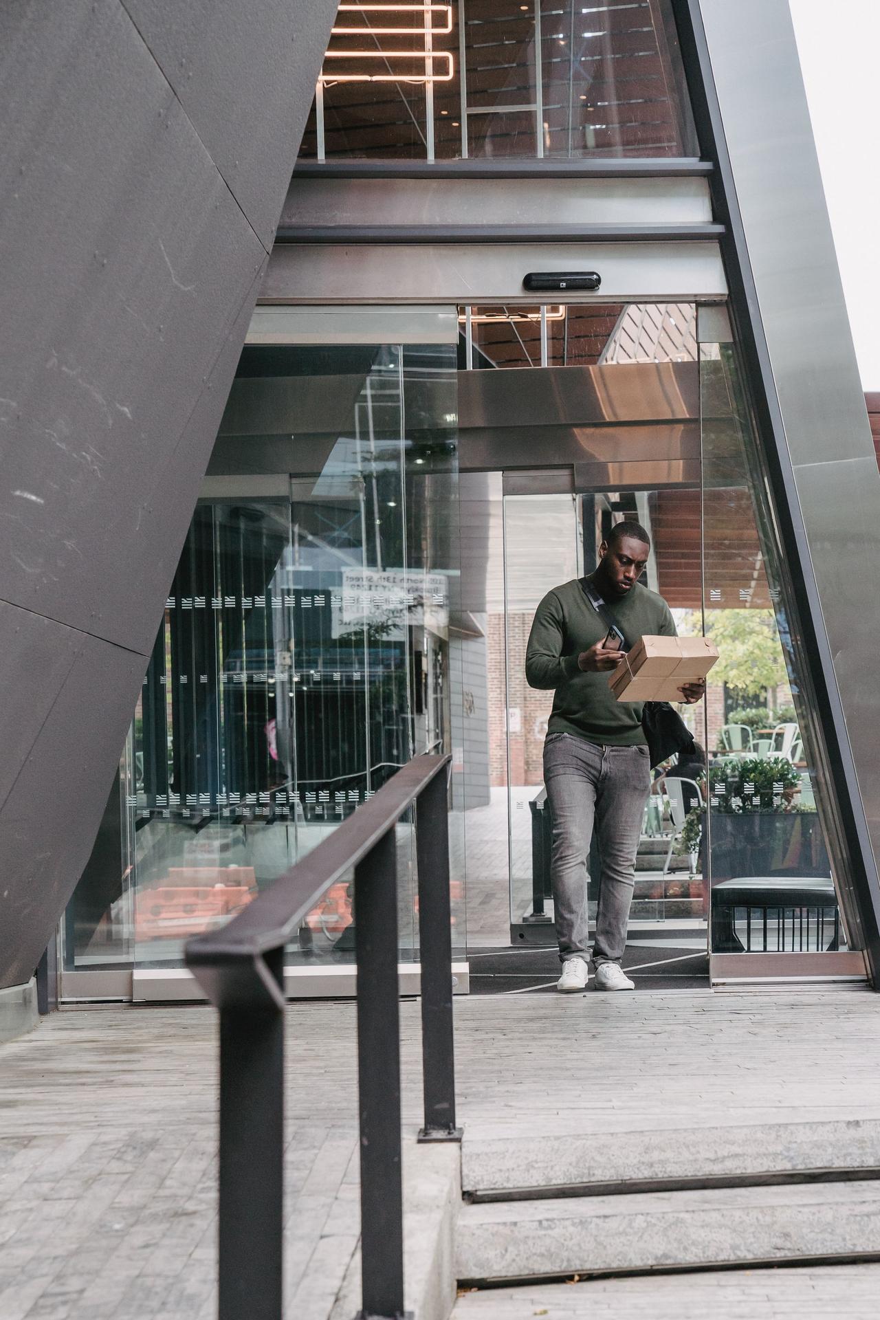 A delivery man using technology outside a modern building. Urban city setting.