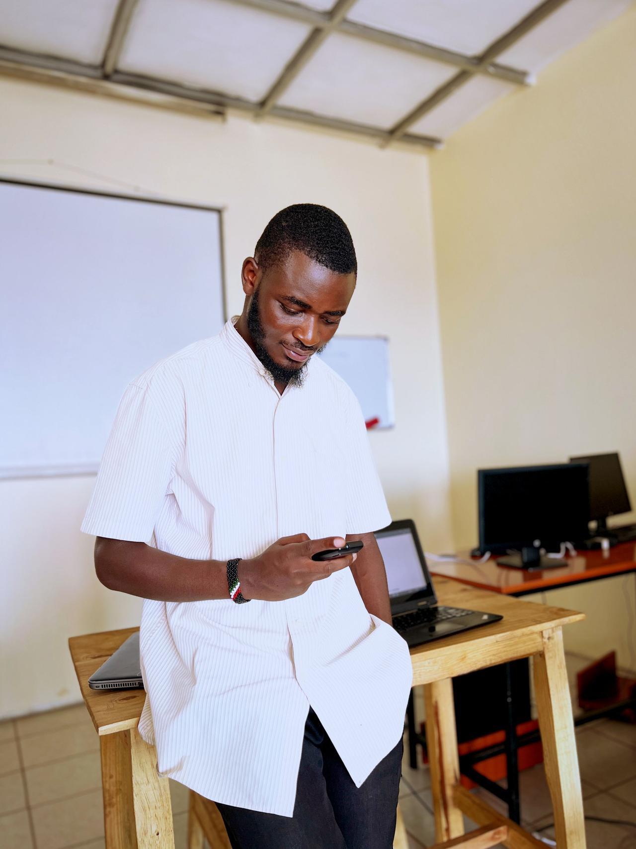 Young man in office environment using smartphone, next to laptop.
