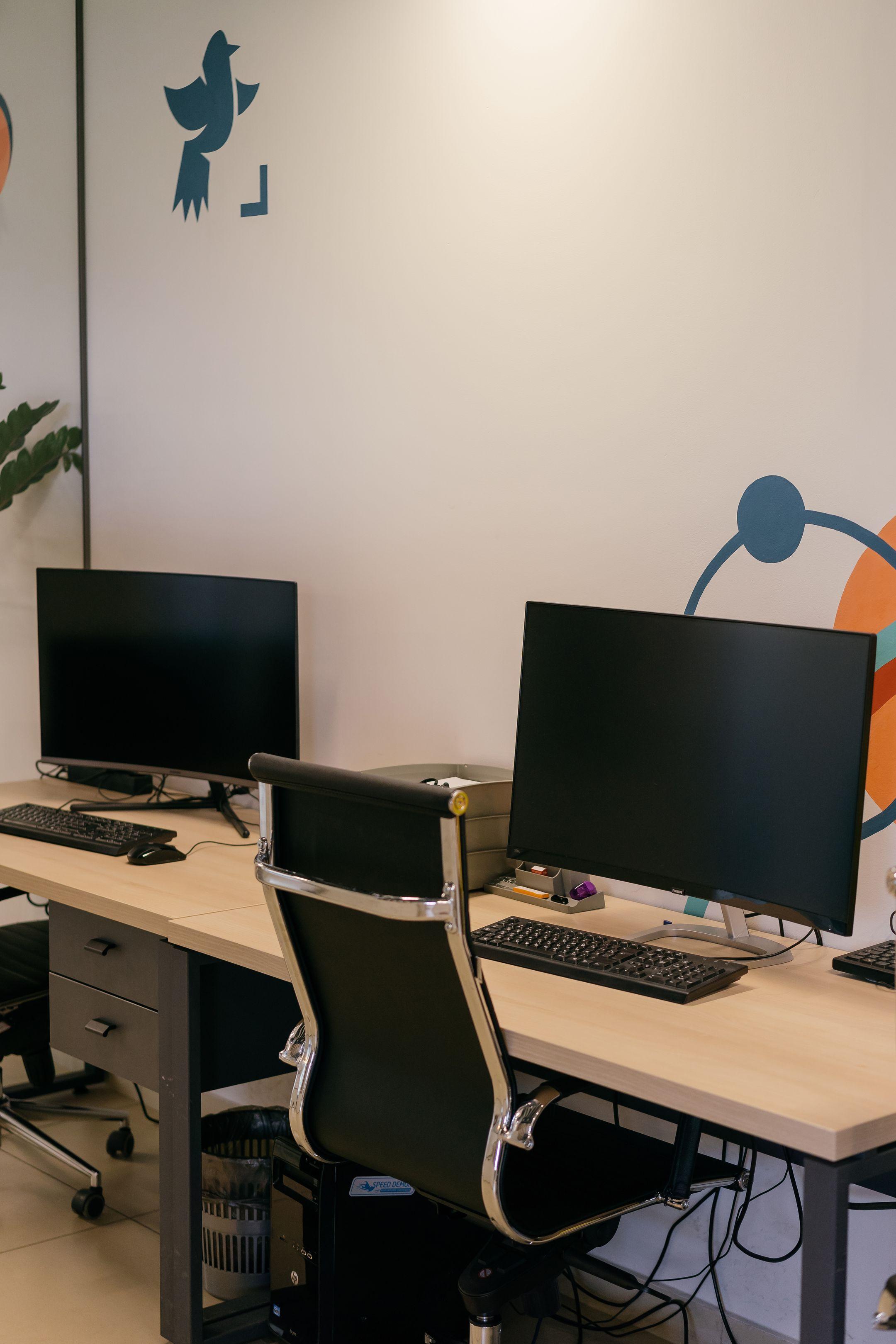 Empty modern office space with two desks, monitors, and stylish chairs.