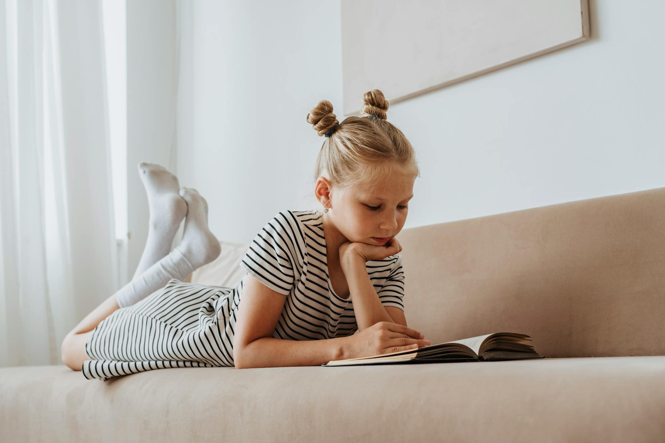 Young girl enjoying a book while lying on a couch, focused and relaxed.