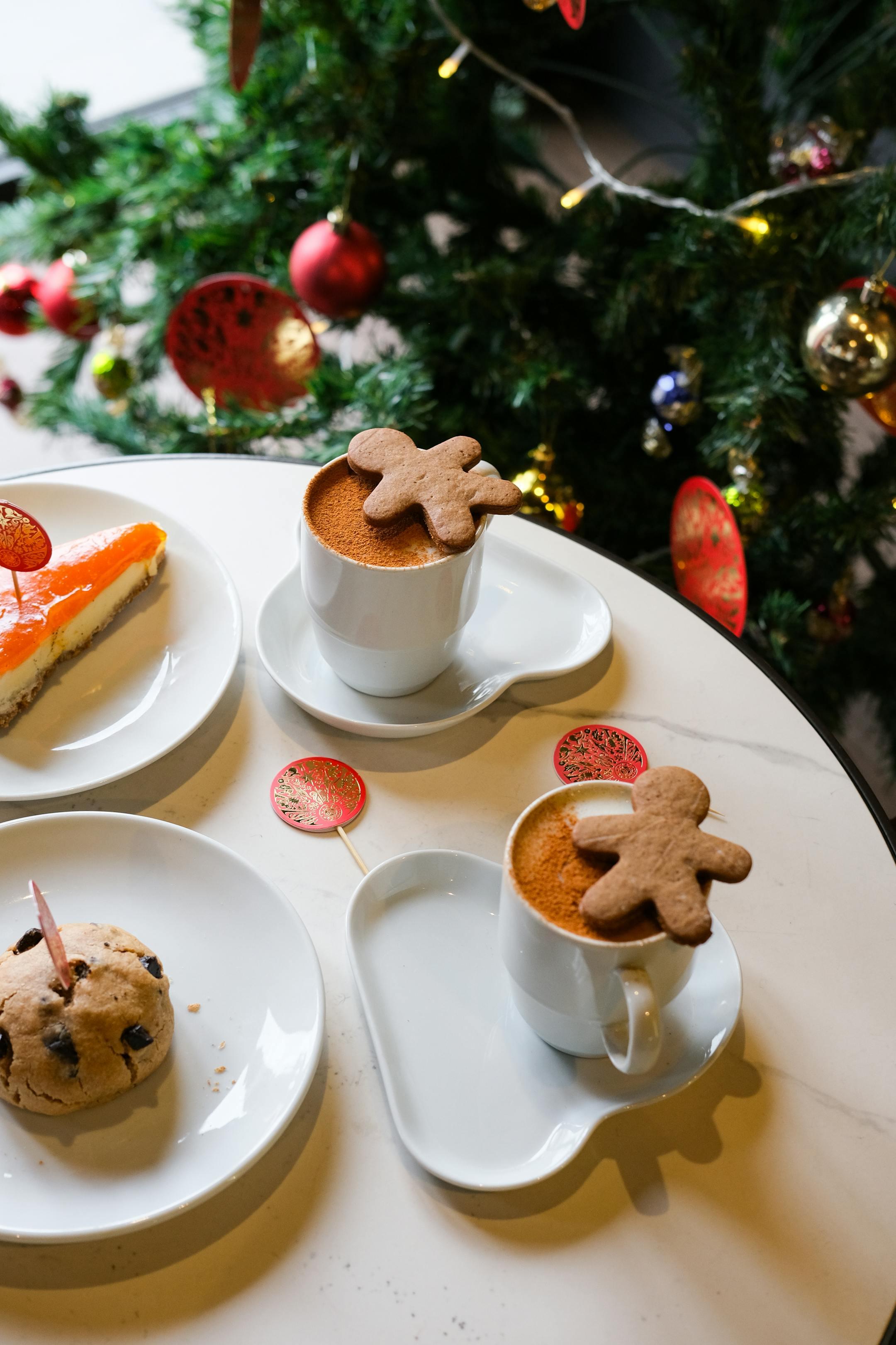 A cozy setup of coffee with gingerbread and holiday treats beside a decorated Christmas tree.