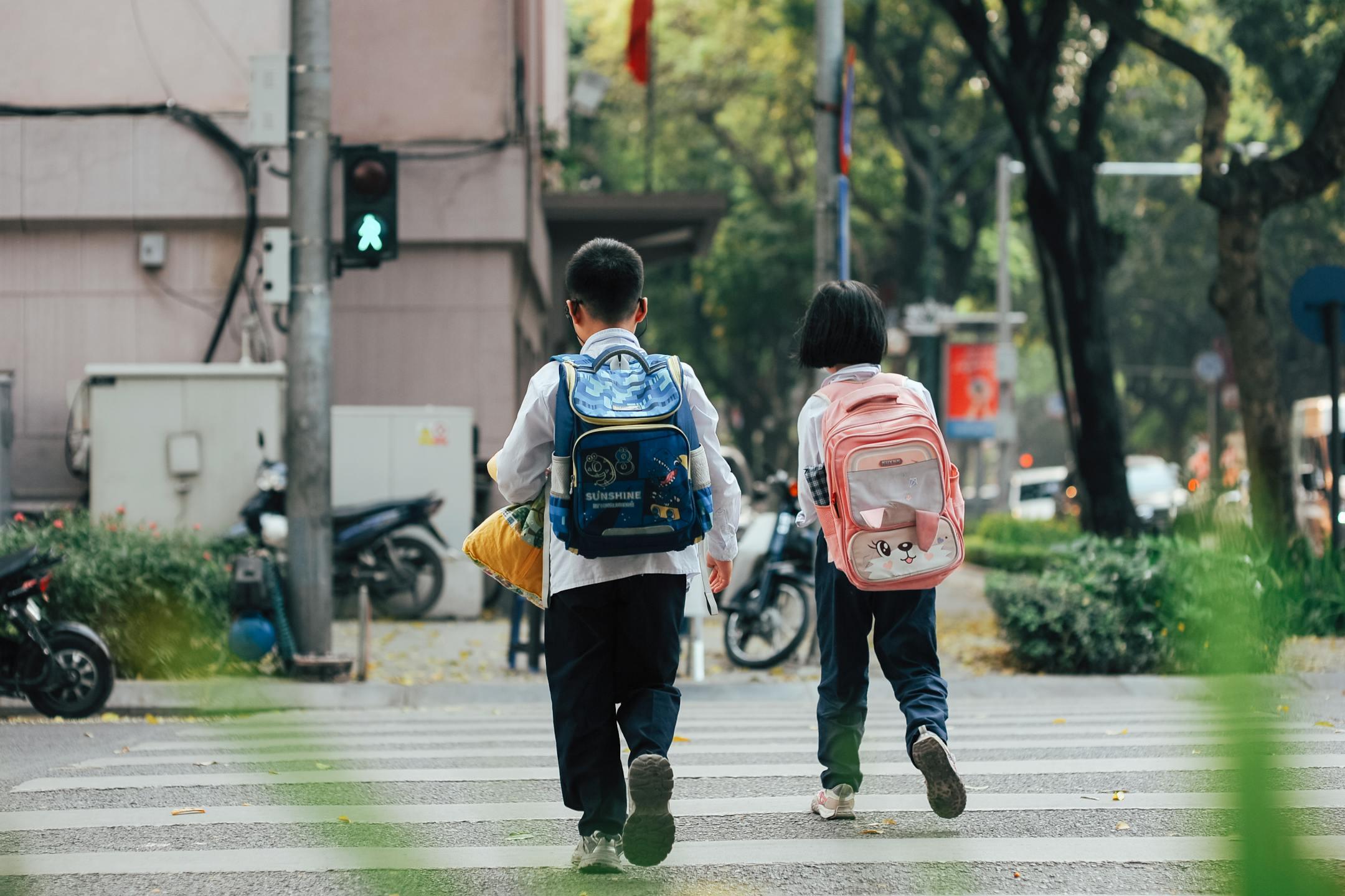 Two children with backpacks crossing a street at a pedestrian crossing.