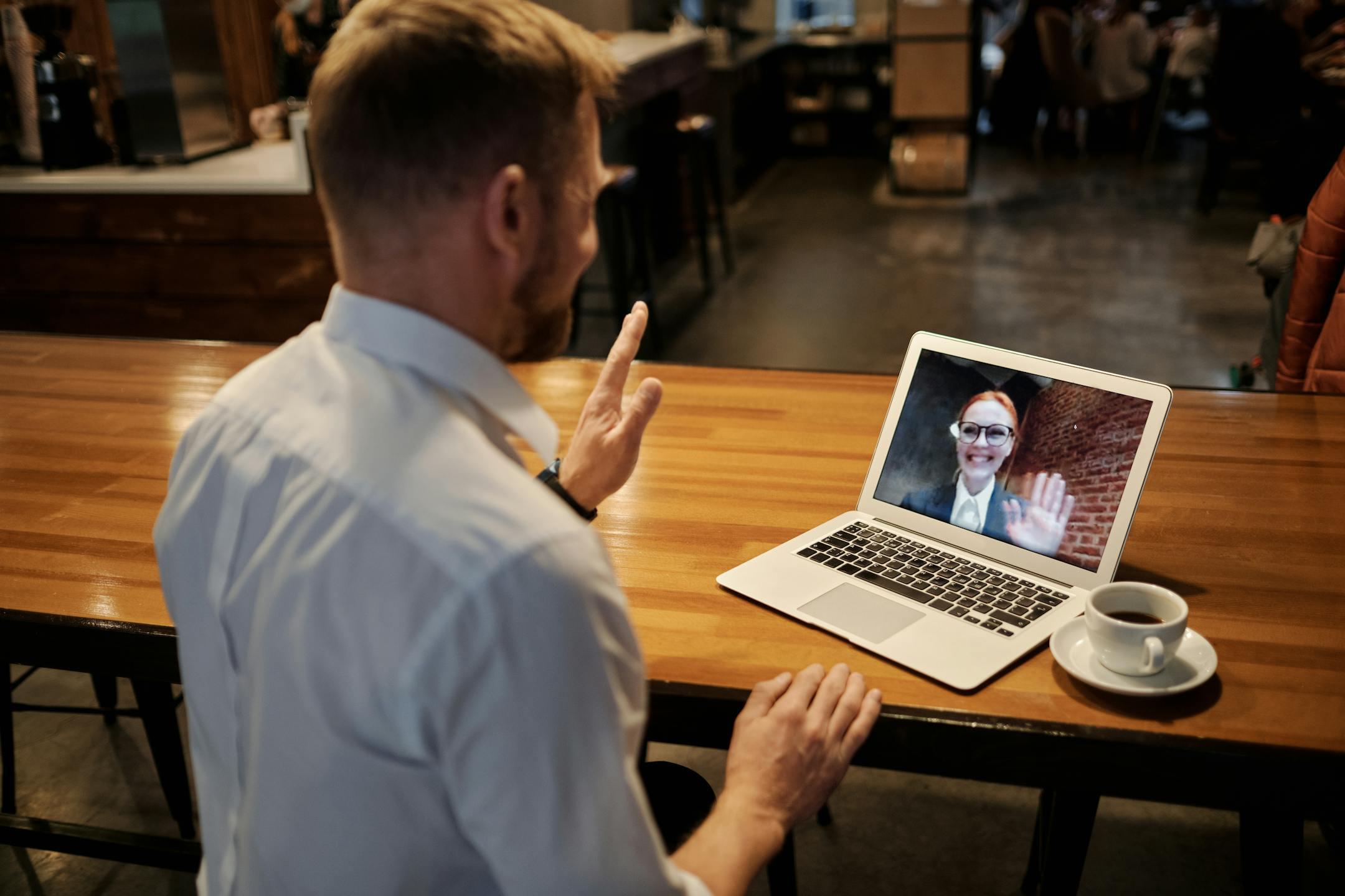 Business meeting conducted virtually in a cozy cafe setting via laptop.