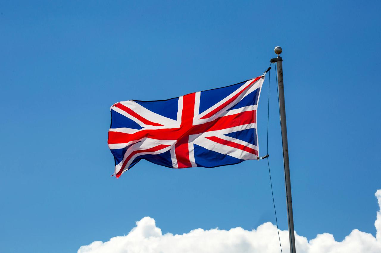 The Union Jack flag of the United Kingdom waving against a clear blue sky.
